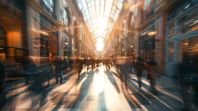 An image of a shopping Mall full of people. The sun is shining through a glass ceiling.