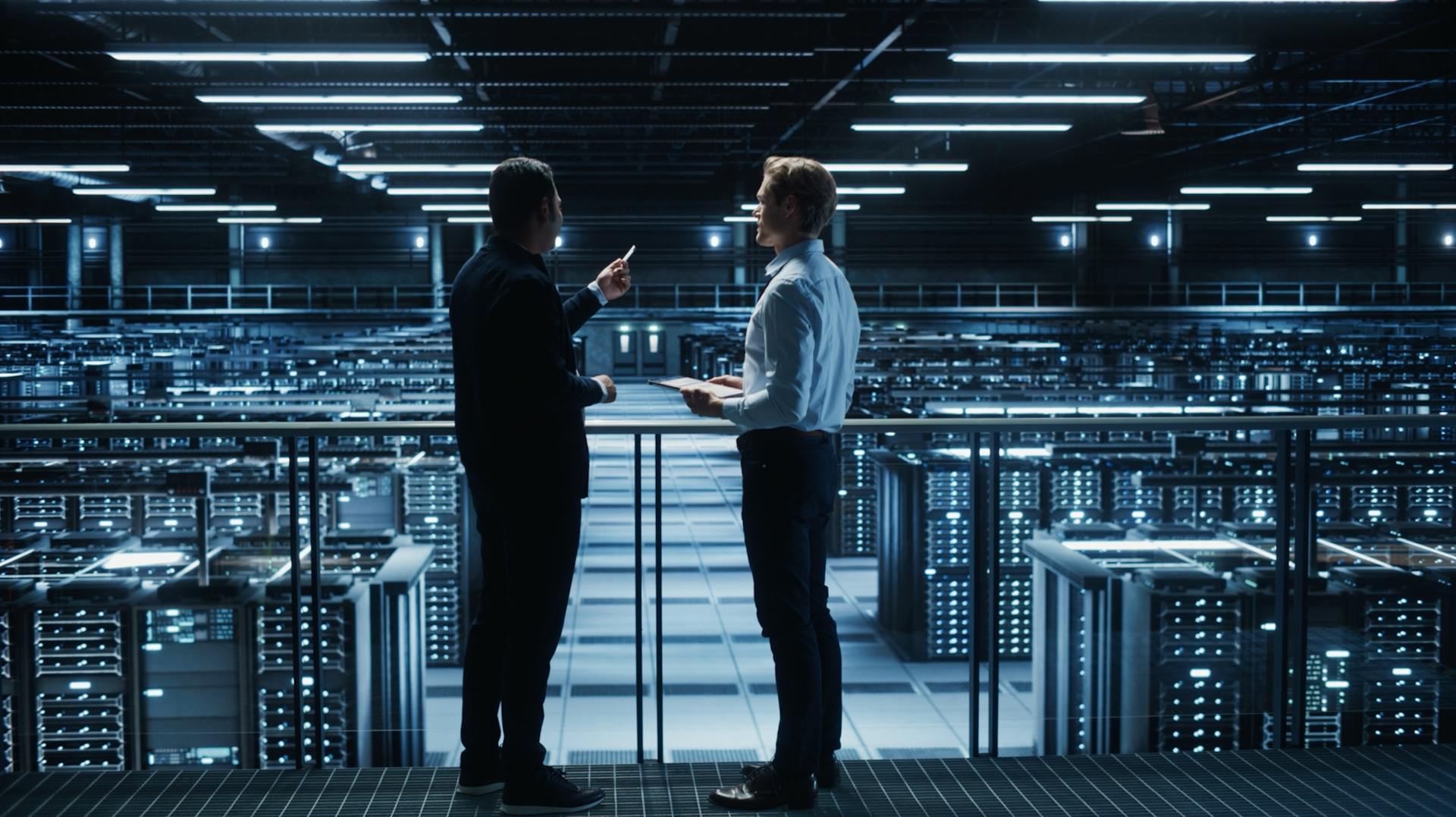 Two men standing on a platform above data centre servers