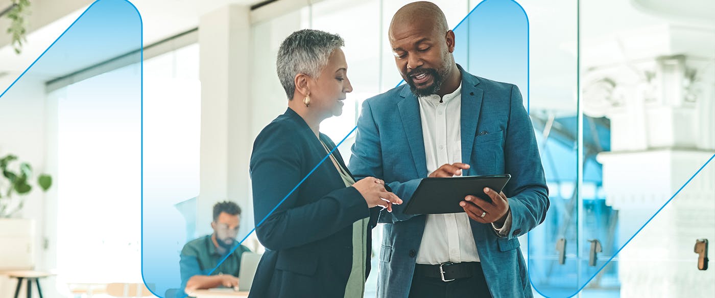 A male a female colleague reviewing work on a tablet while standing a bright modern office