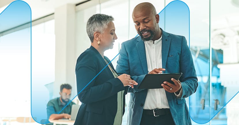 A male a female colleague reviewing work on a tablet while standing a bright modern office 