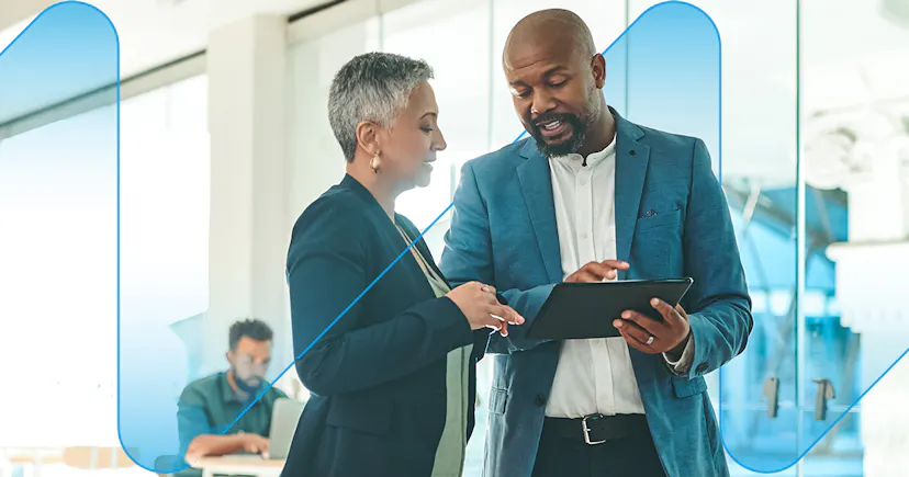 A male a female colleague reviewing work on a tablet while standing a bright modern office