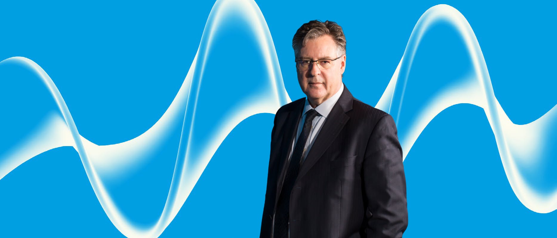 image of a man with grey hair and glasses wearing a suit on a blue background with a white swirl