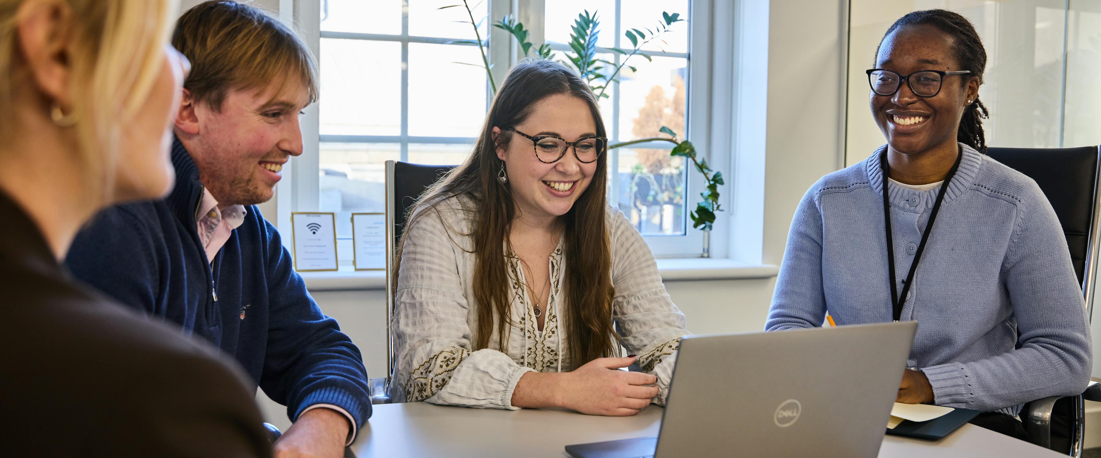 image of three women and a man at a meeting room table with laptop