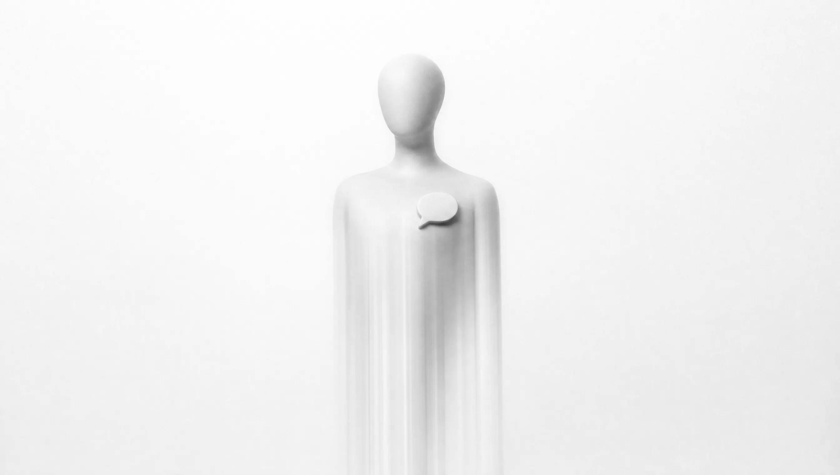 Fotografia in bianco e nero a lunga esposizione di un busto-manichino bianco senza volto, con un piccolo fumetto in rilievo sul petto; la testa e le spalle sono nitide, mentre dal busto in giù la figura si dissolve in scie verticali di luce su fondo quasi bianco