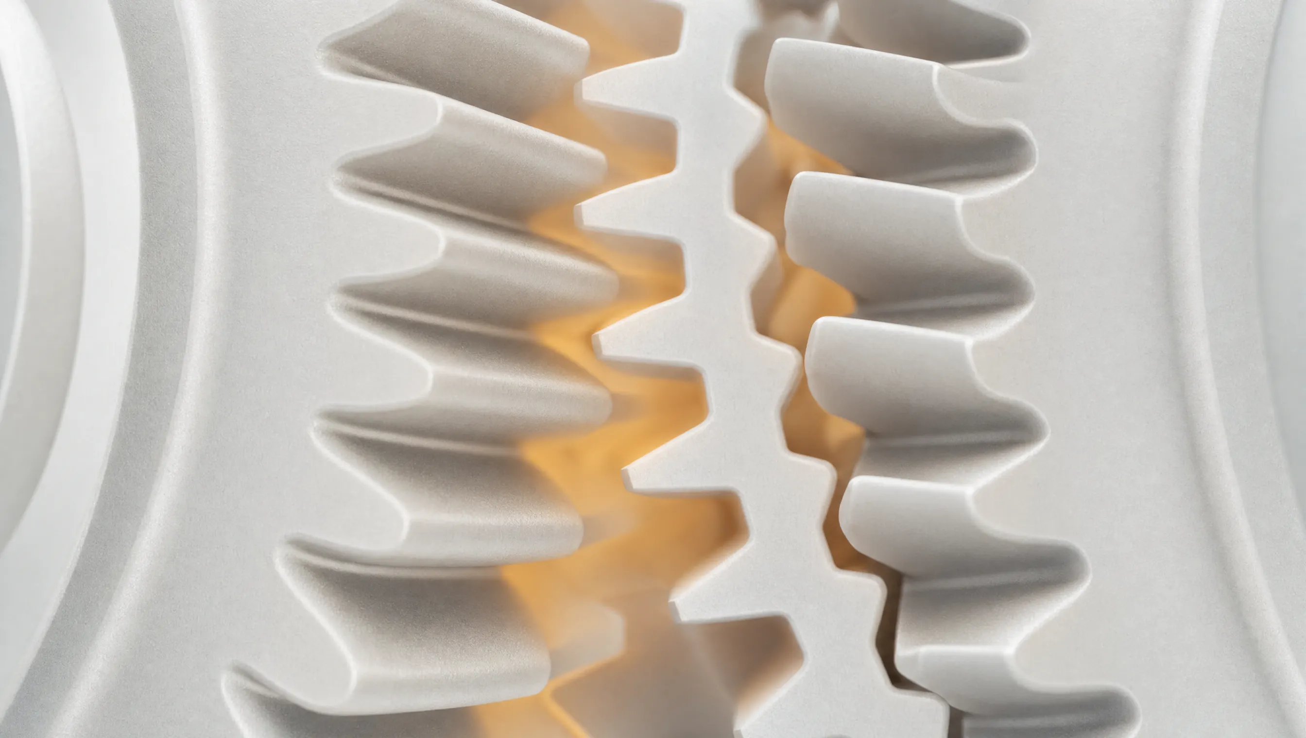Macro di denti di ingranaggio in materiale bianco opaco: a sinistra si incastrano, a destra restano disallineati, con un bagliore ambra al centro