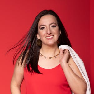Mulher branca, cabelo castanho médio, utilizando batom rosa e sorrindo de perfil em um fundo verde claro.'