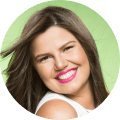 Mulher branca de cabelo liso e castanho, batom rosa nos lábios, sorrindo.