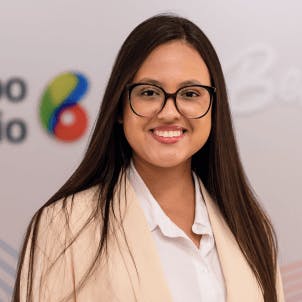 Mulher de cabelo escuro e longo, óculos de grau com armação arredondada, sorrindo.