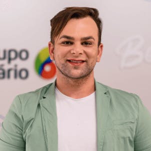 Homem de cabelo curto castanho médio, maquiagem leve e barba por fazer sorrindo