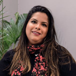 Mulher de cabelo longo e escuro com mechas claras nas pontas, com maquiagem leve e sorrindo