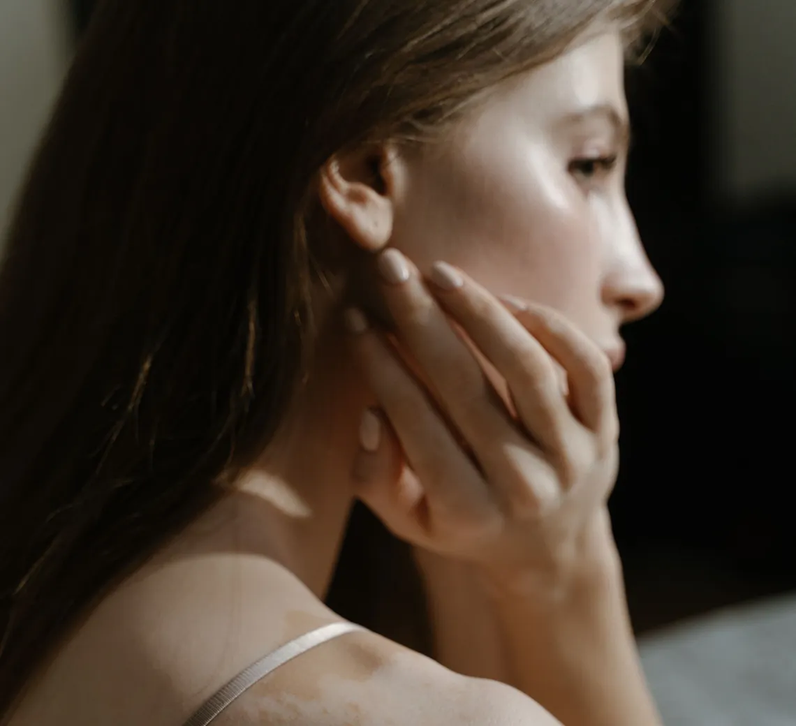 Une jeune femme touche sa joue près d’une fenêtre.