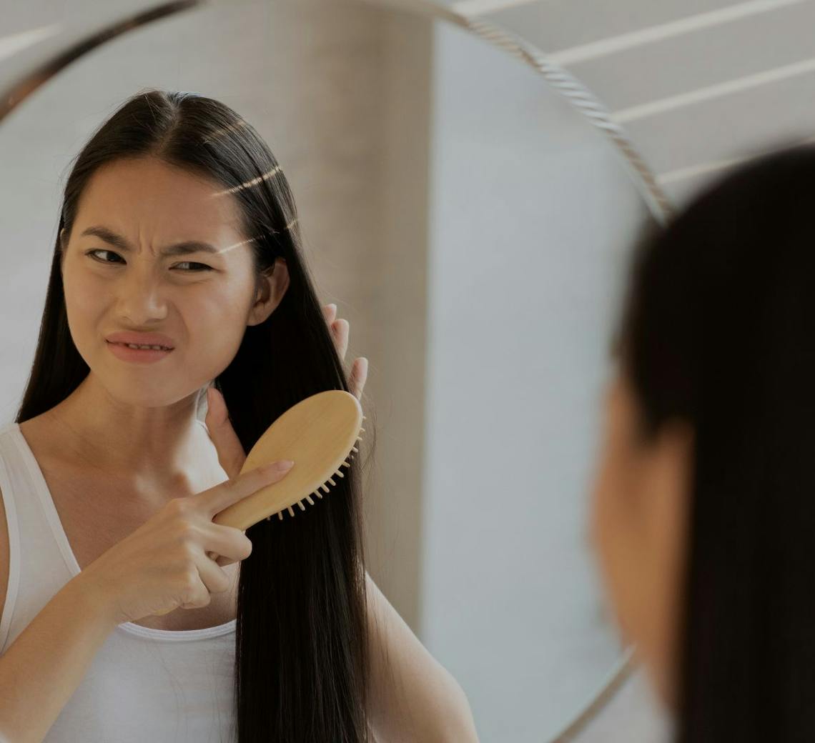 Jeune femme qui se regarde dans le miroir suite à une chute de cheveux.