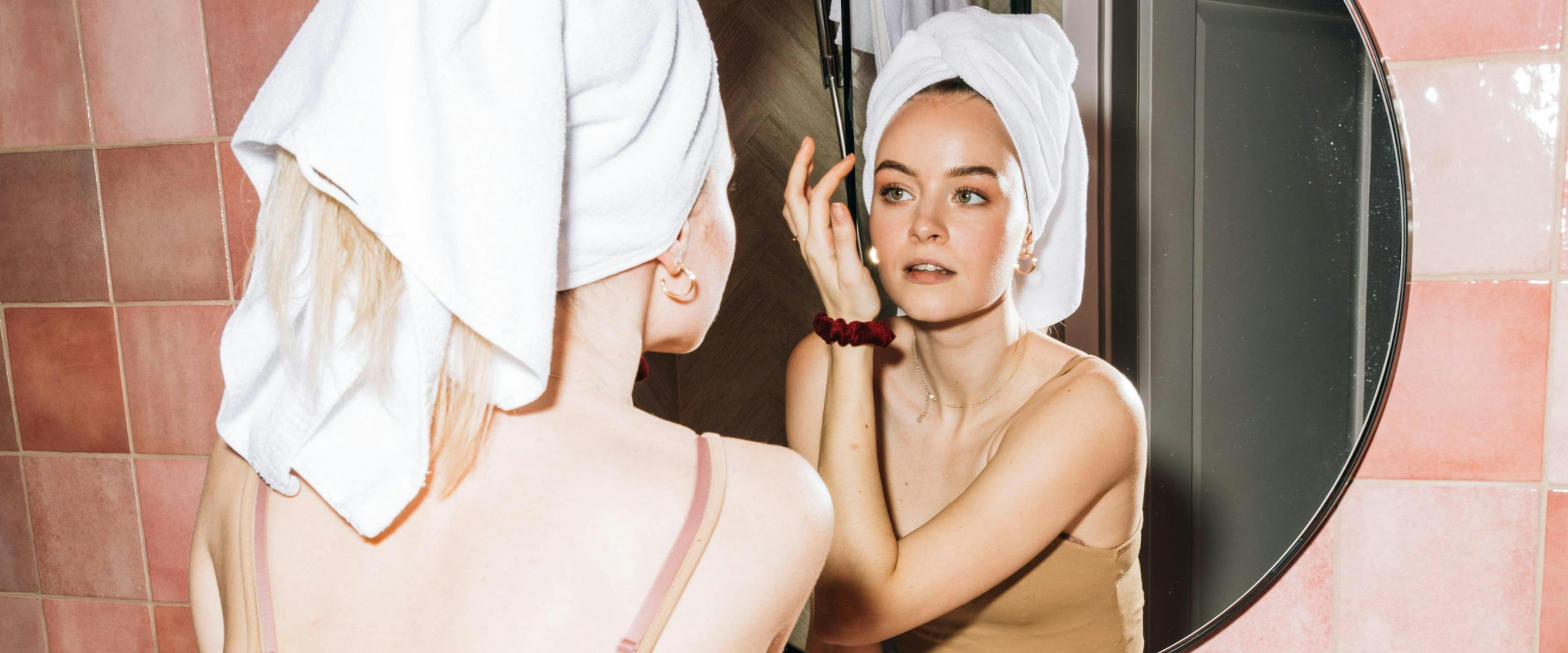 Jeune femme qui se regarde dans le miroir le visage et la peau.