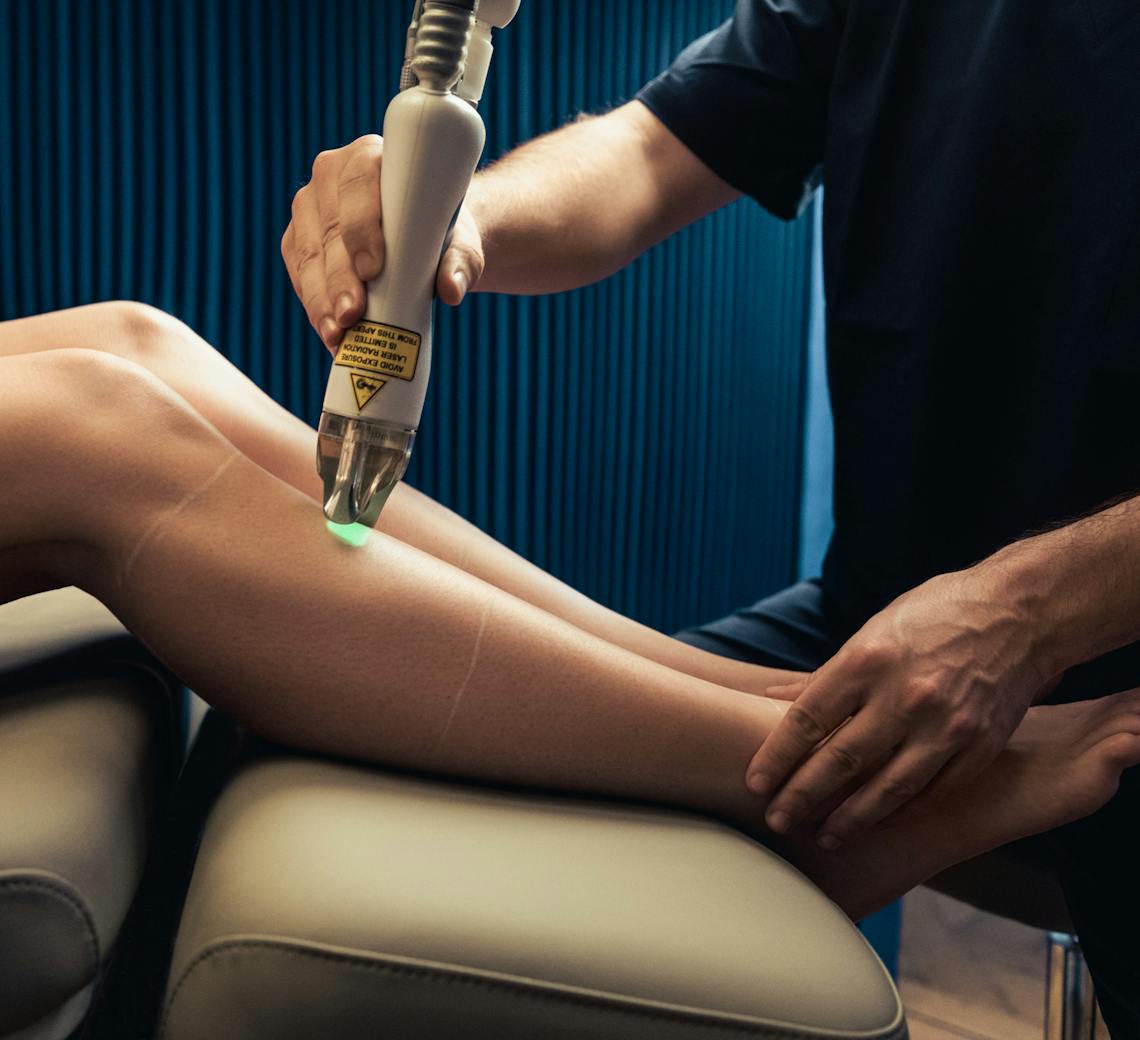 Praticien qui réalise une épilation laser sur les jambes d'une patiente lors d'une consultation.