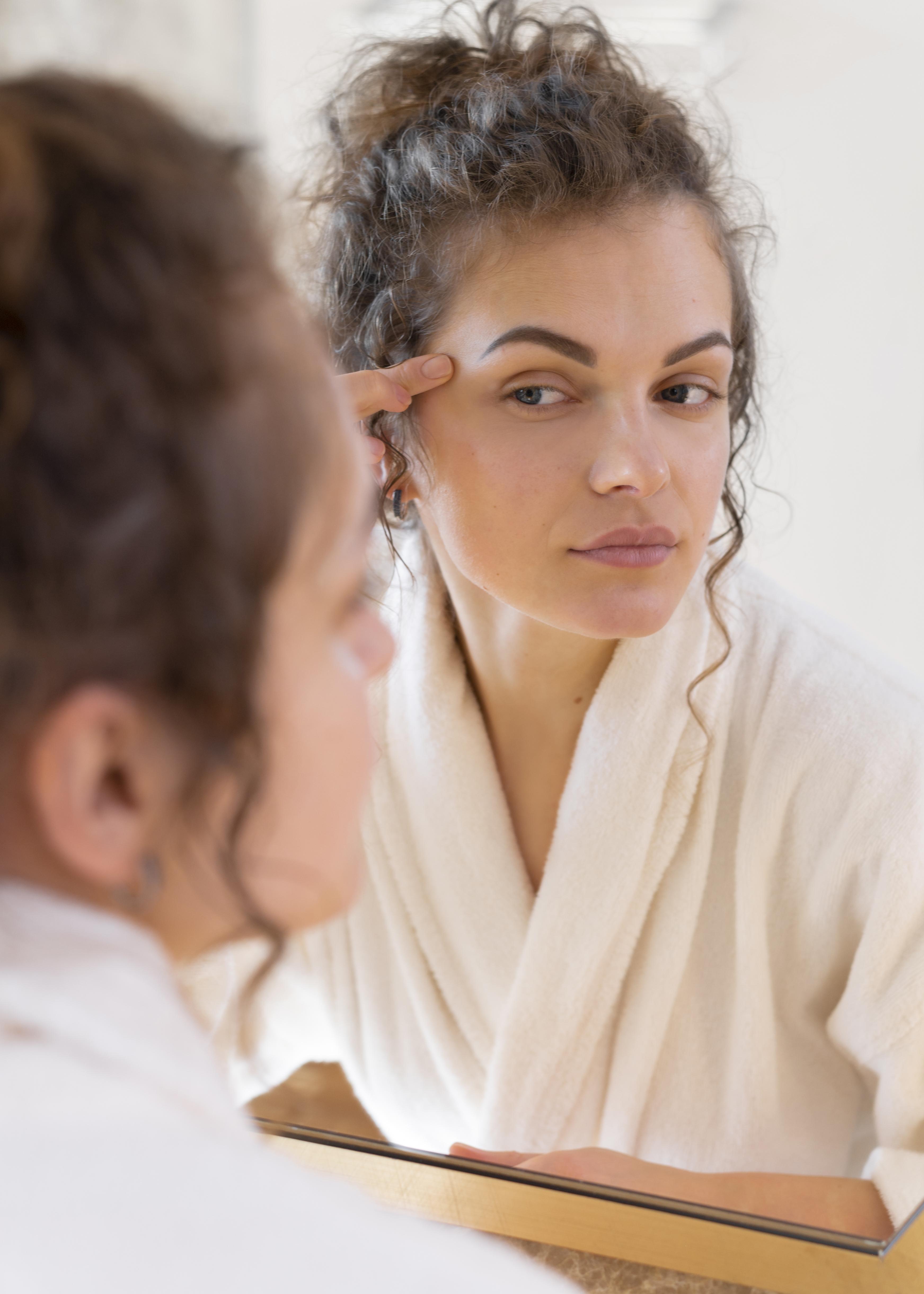 Jeune femme qui regarde sa peau dans le miroir