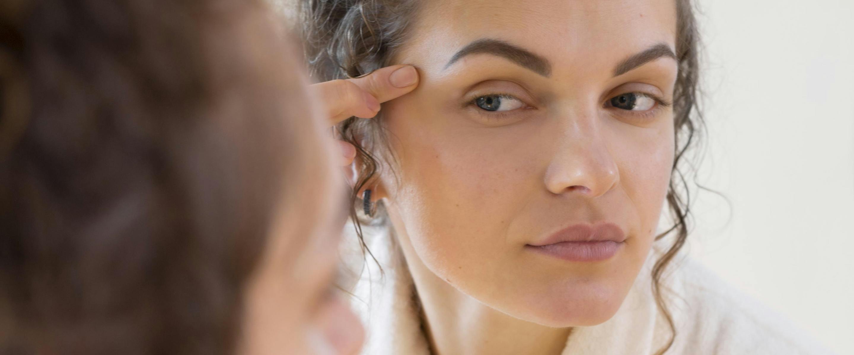 Jeune femme qui regarde sa peau dans le miroir
