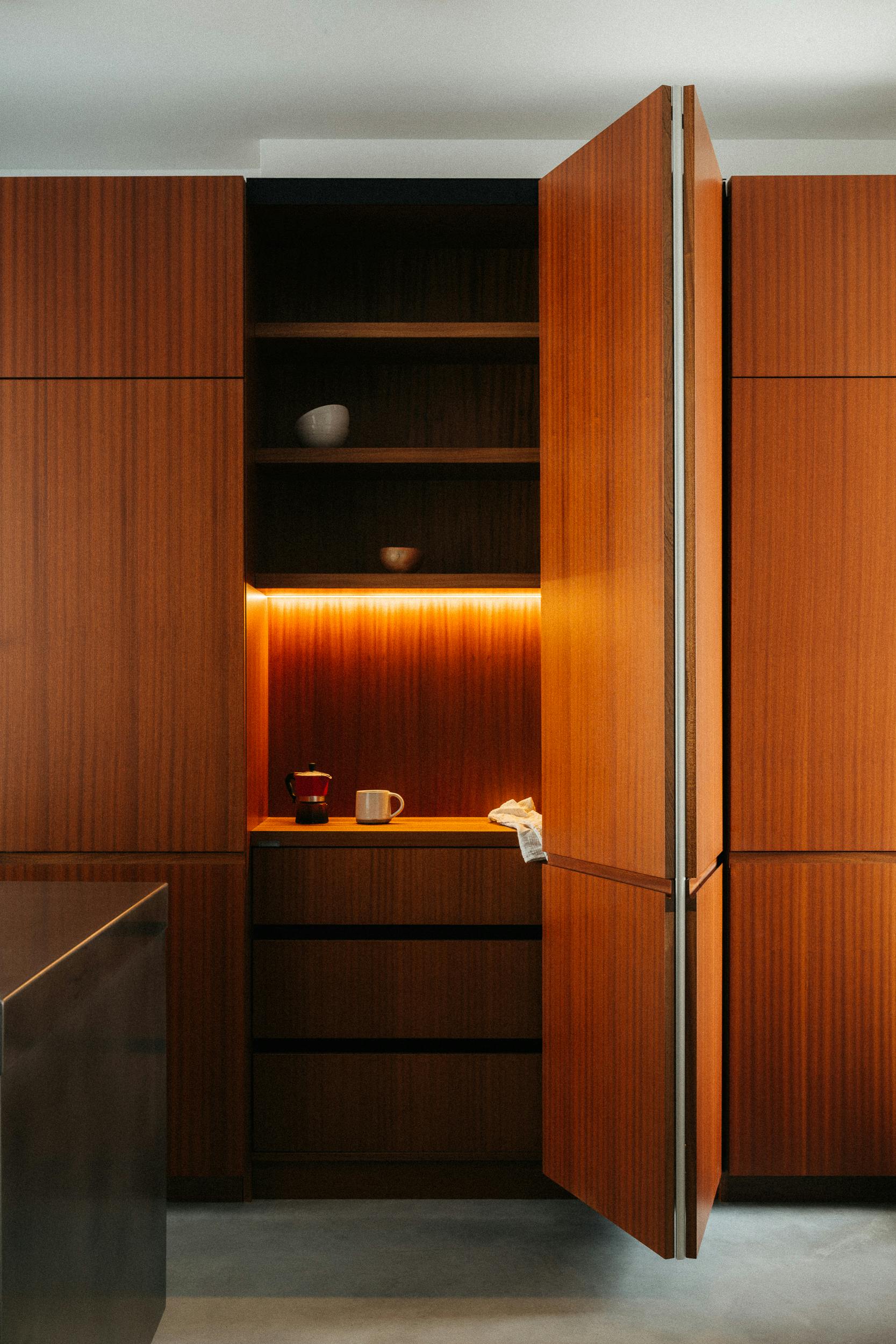 Tall storage kitchen cupboard with integrated lighting in our dark timber Ma-kon kitchen.
