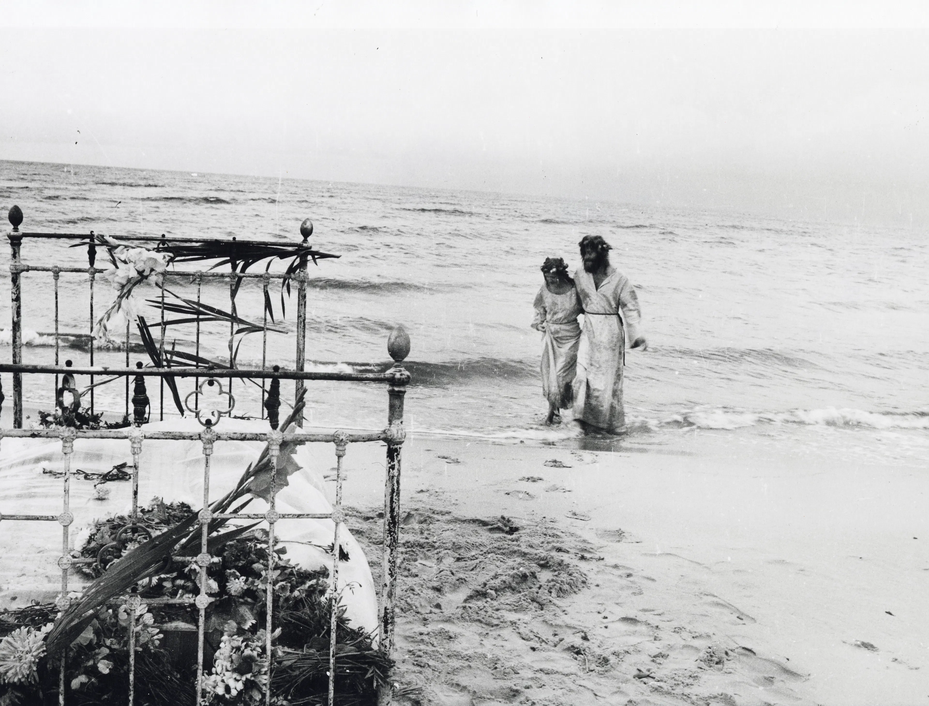 The photograph shows a woman and a man, resembling Jesus, walking along the seashore. On the left side of the picture is a bed decorated with flowers.