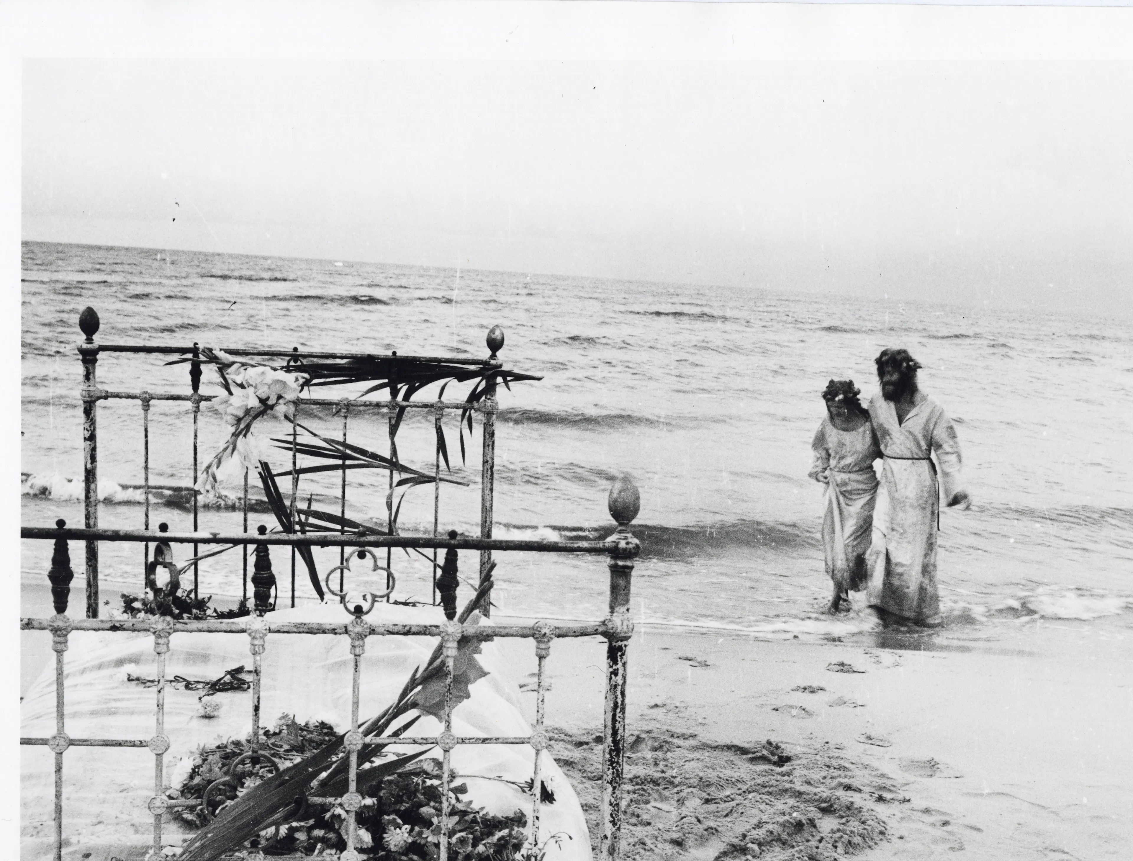 The photograph shows a woman and a man, resembling Jesus, walking along the seashore. On the left side of the picture is a bed decorated with flowers.