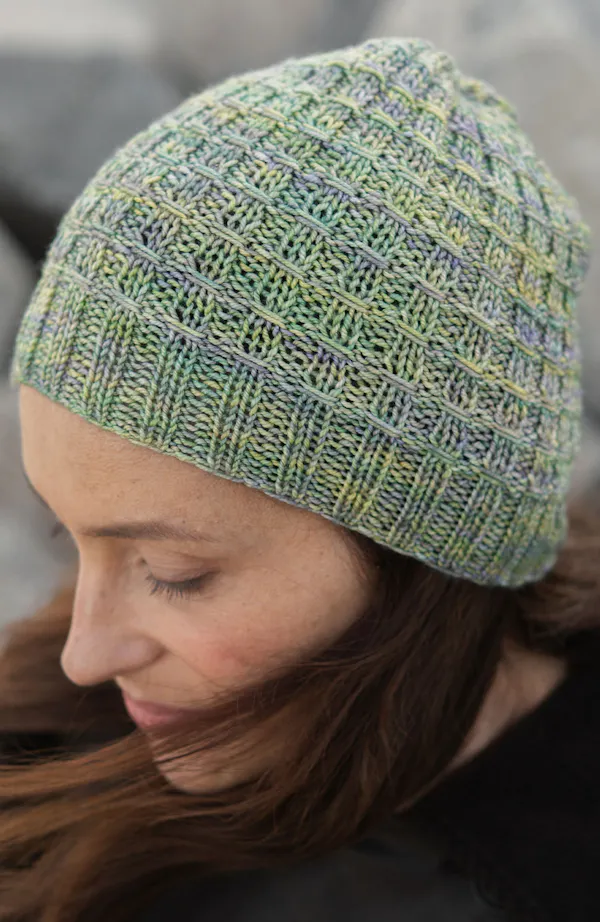 Picture of Brisa Knit Hat: A textured, hand-knit beanie crafted in a soft variegated yarn featuring subtle tones of sage green, pale lavender, and light yellow, knitted in a grid-like ribbed pattern with a neat ribbed brim.