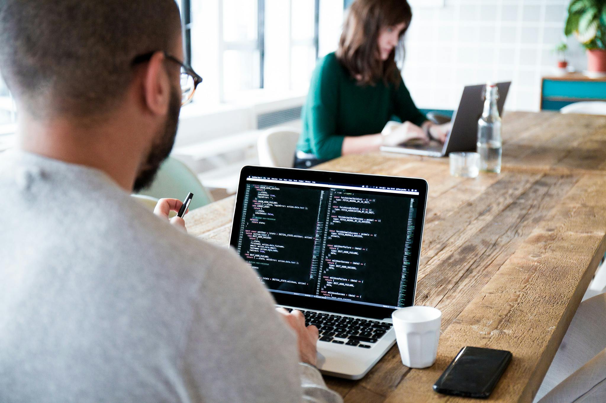 Man coding on his laptop, making a website, man sitting behind a desk typing on his laptop
