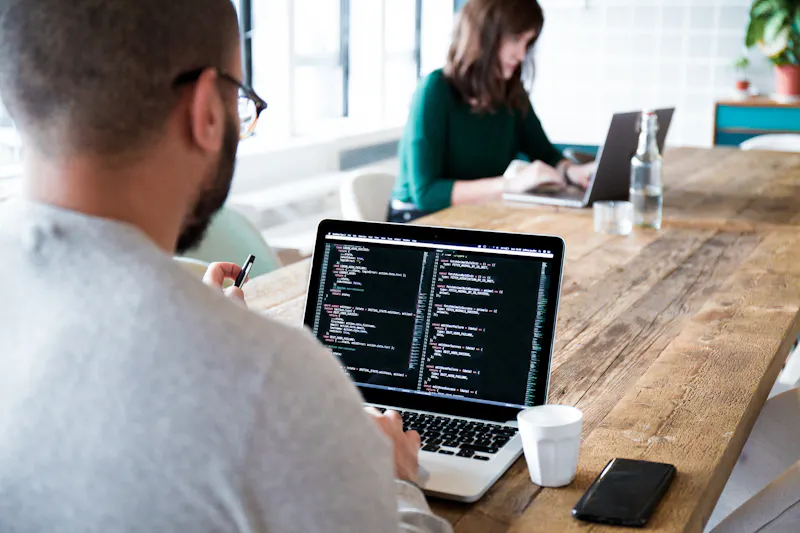 Man coding on his laptop, making a website, man sitting behind a desk typing on his laptop