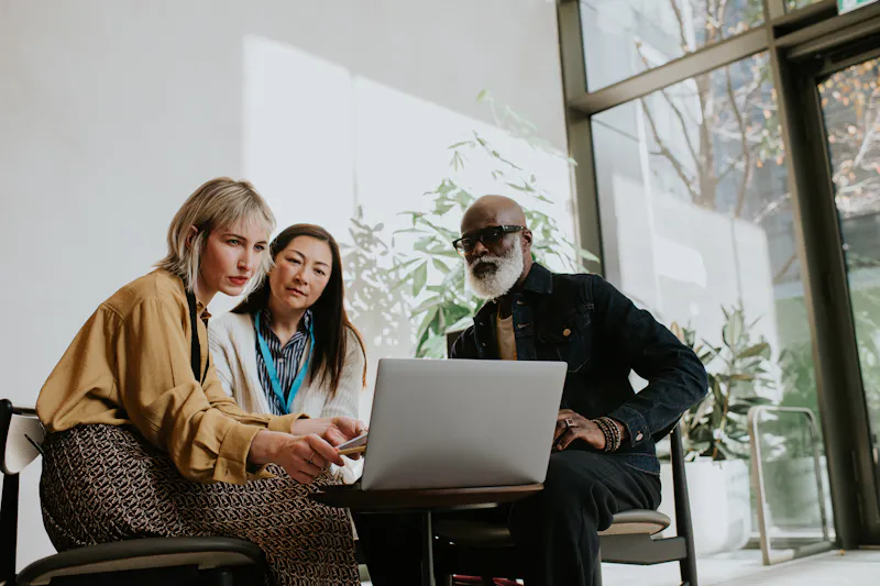 three people sitting around a laptop looking a the screen. marketing strategies.