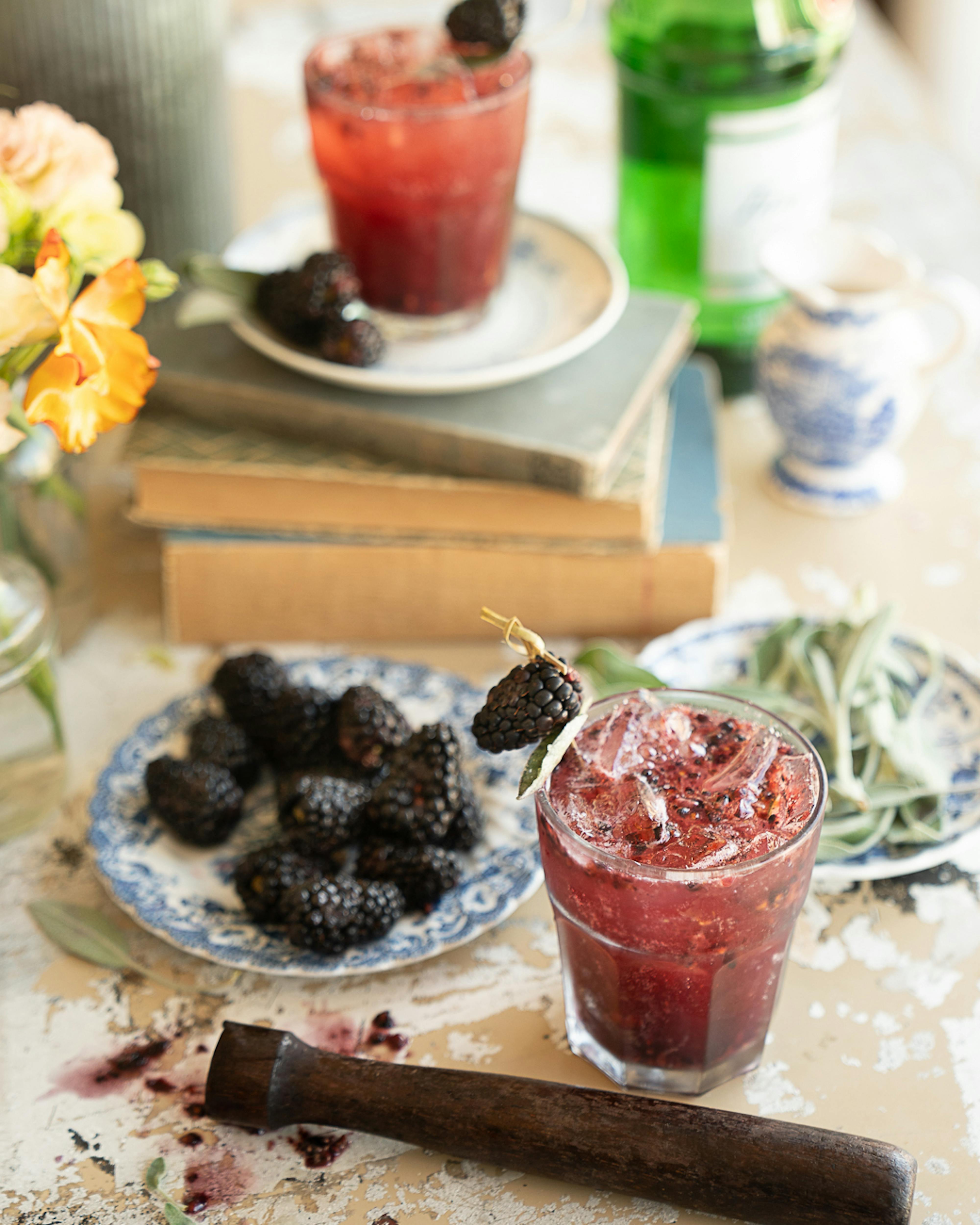 blackberry sage smash on table with blackberries, sage, and muddling stick