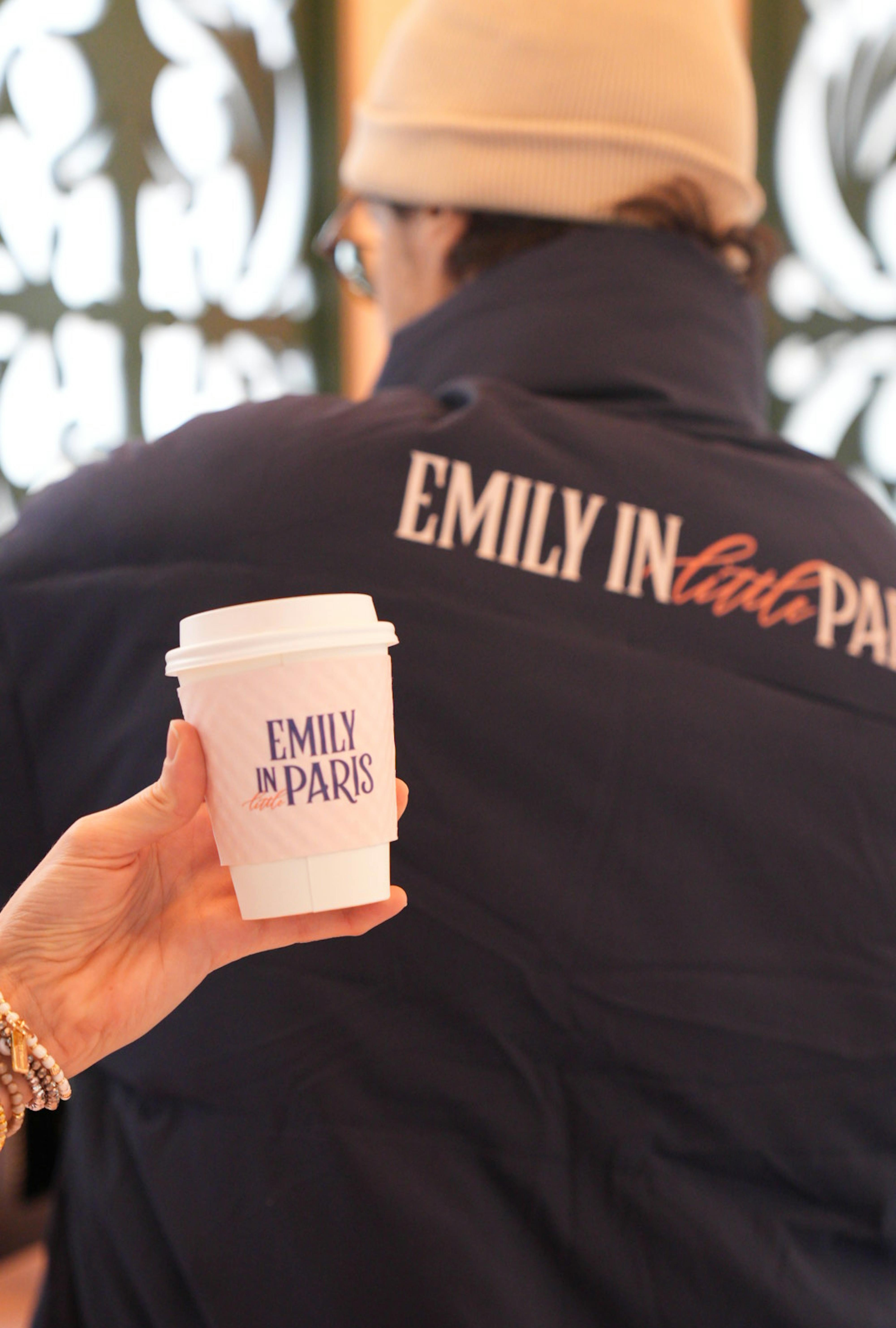 woman holding up emily in little paris branded cup as man pours a hot cocoa