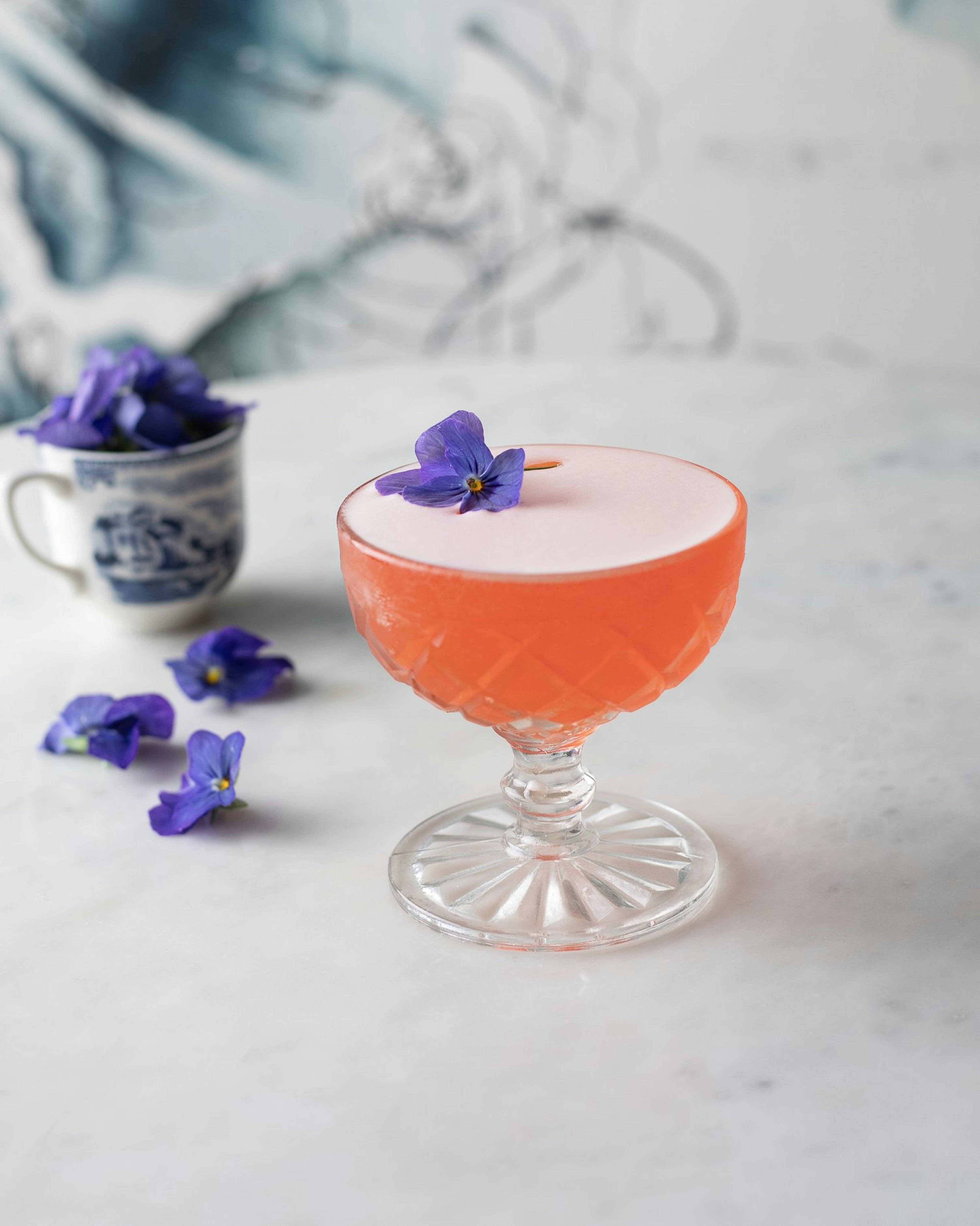 aperol martini with an edible purple flower as a garnish
