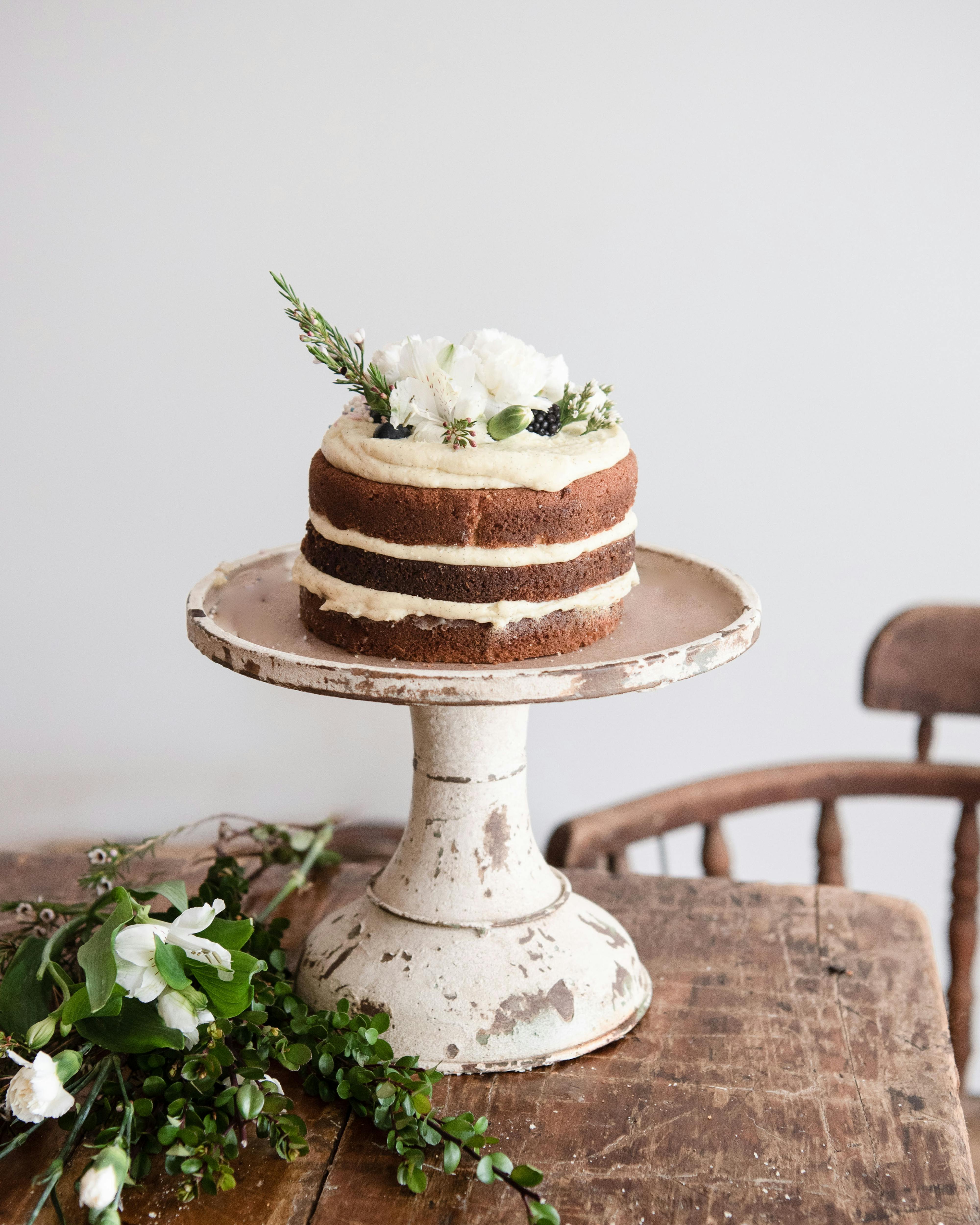 rustic naked cake on antique cake stand with white flowers on top

