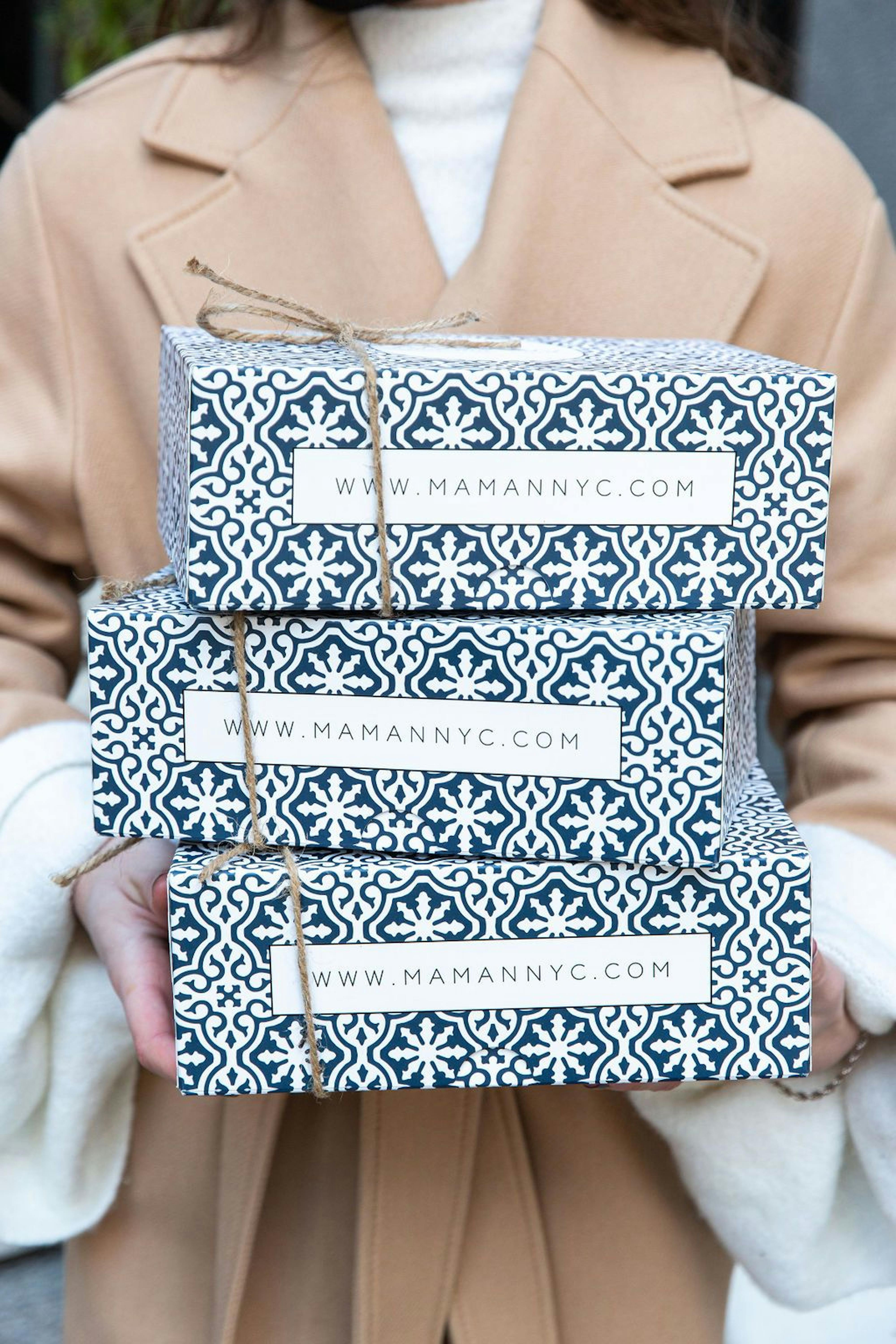 woman in winter coat holding three cookie boxes