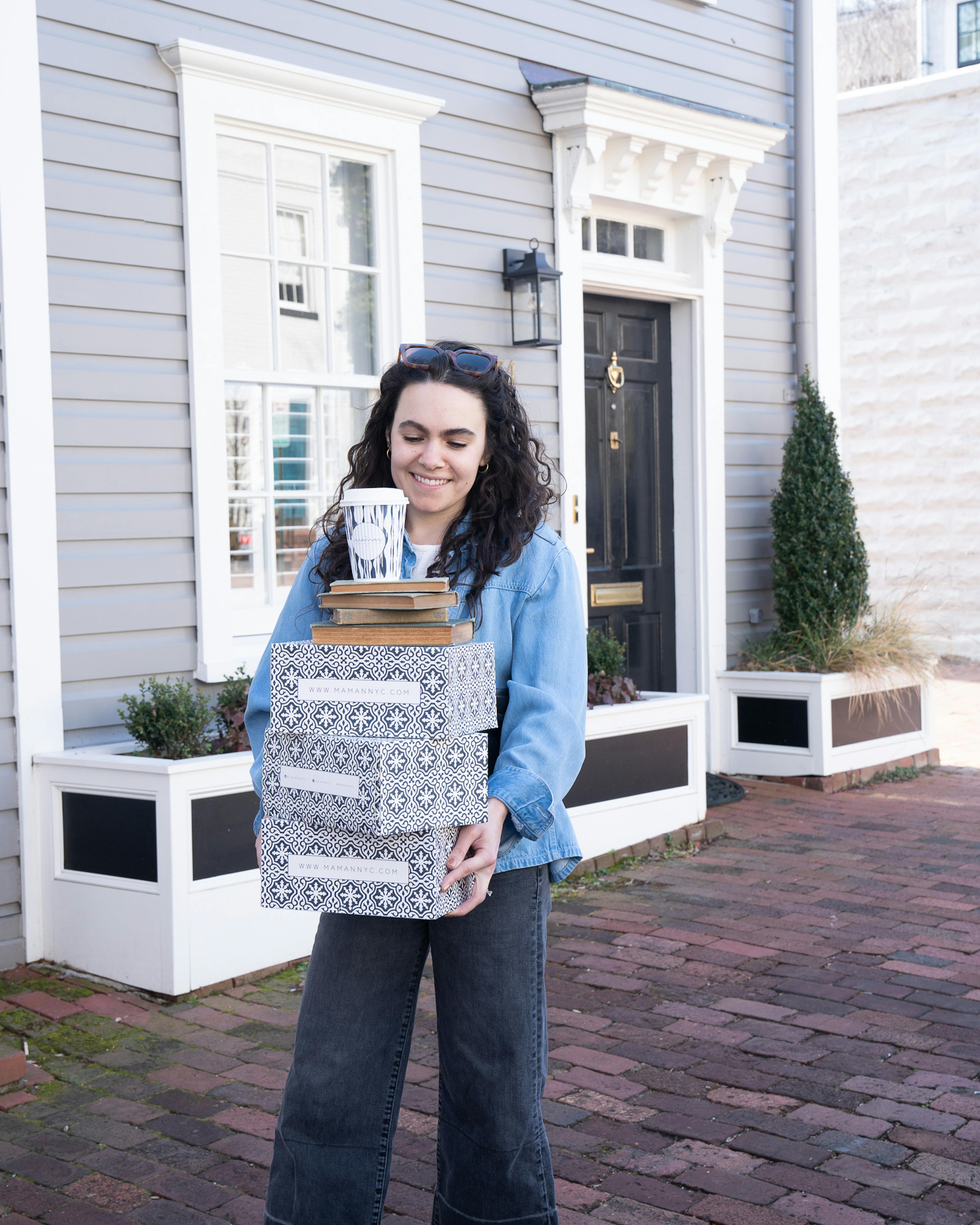 woman holding stack of maman cookie boxes outside of ornate townhouse