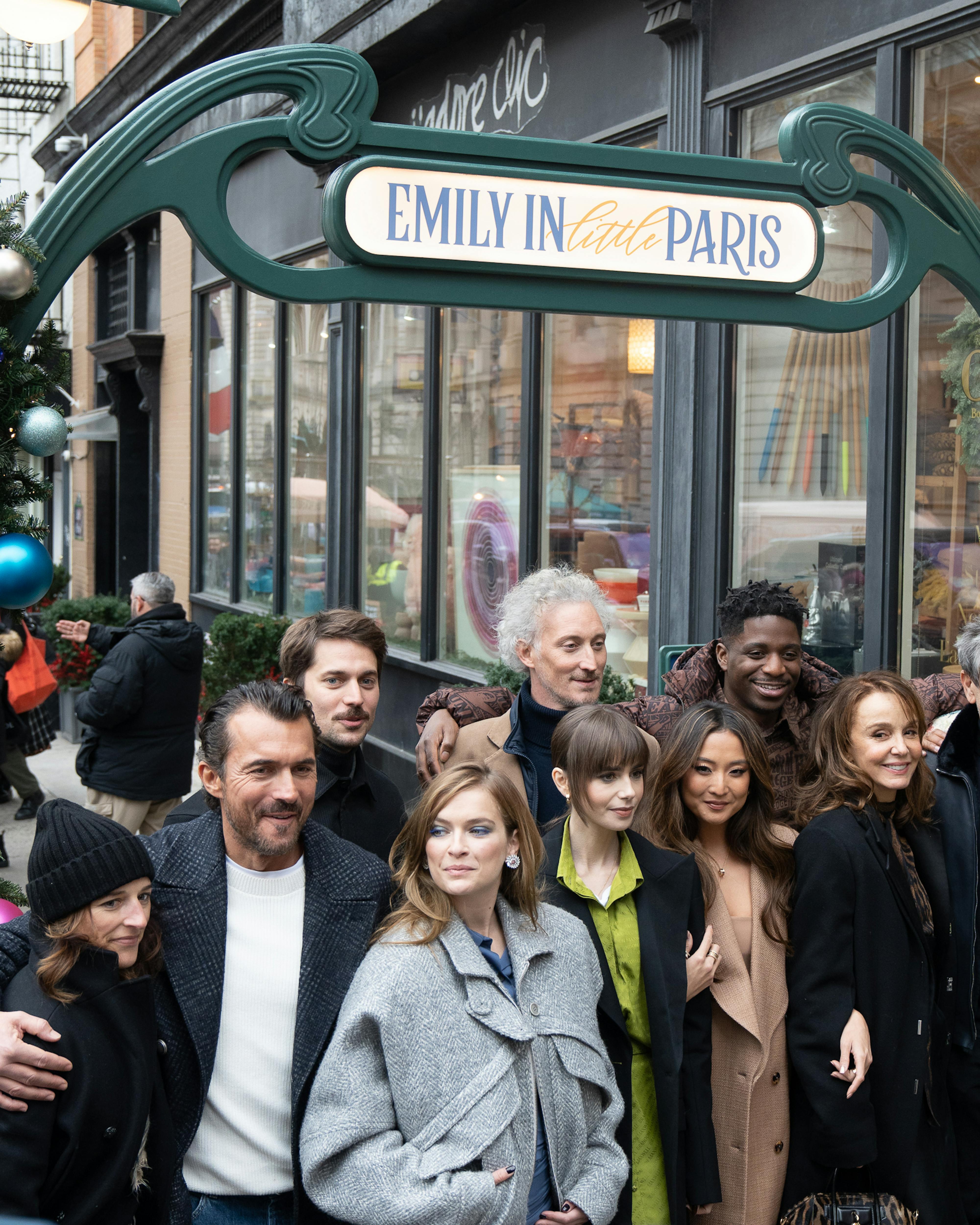 the entire cast of emily in paris outside of little paris popup sign 