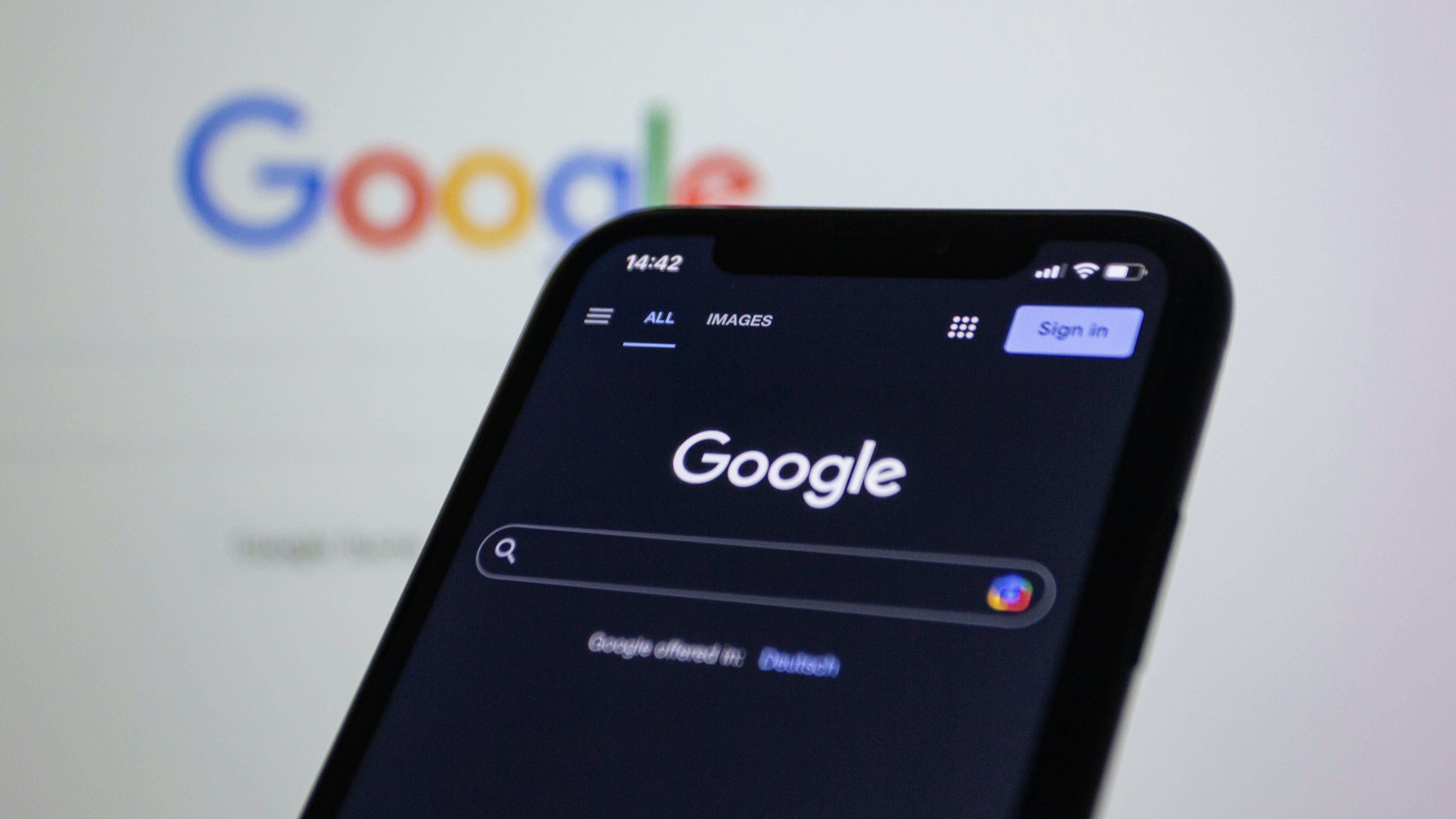 Smartphone affichant la page de recherche Google, logo Google flouté en arrière-plan sur écran d'ordinateur