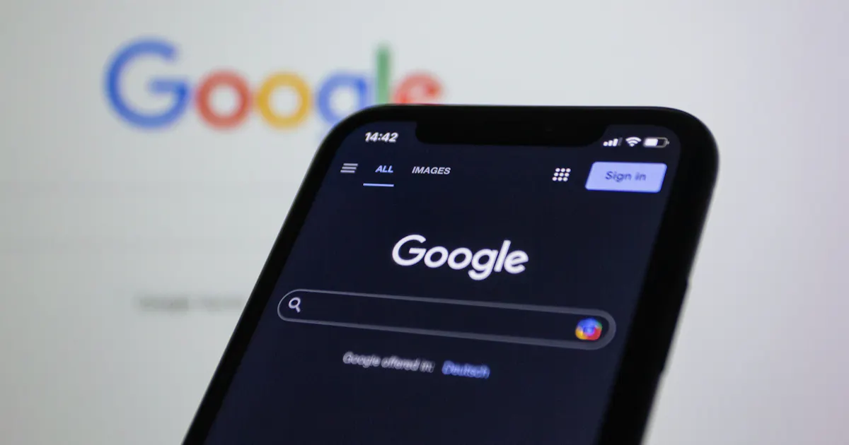 Smartphone affichant la page de recherche Google, logo Google flouté en arrière-plan sur écran d'ordinateur