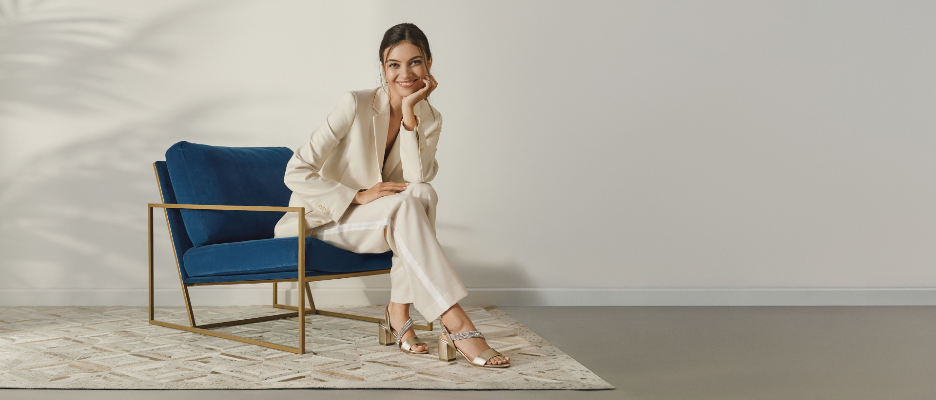 Kobieta siedzi na niebieskim fotelu i ma na sobie złote sandałki.