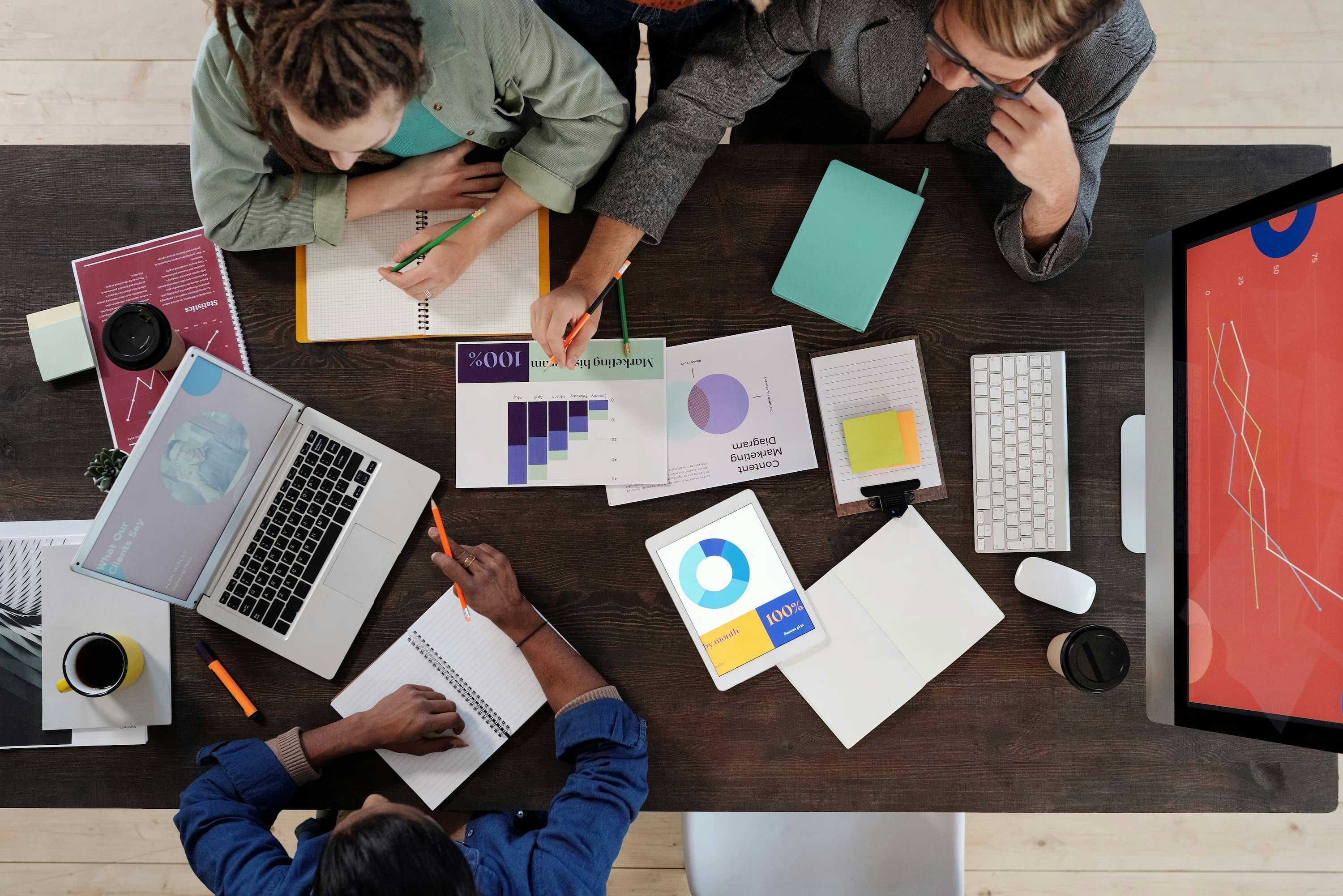 group of people sitting around a table with paper and laptops