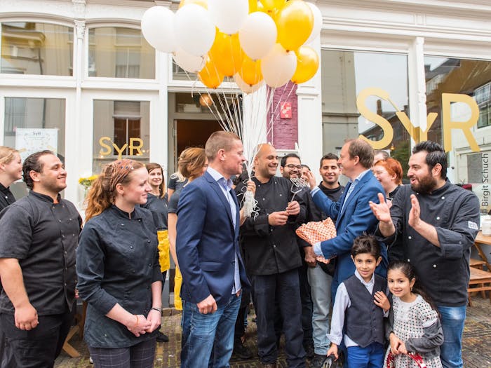 Photograph of the opening party with people celebrating in front of the restaurant.