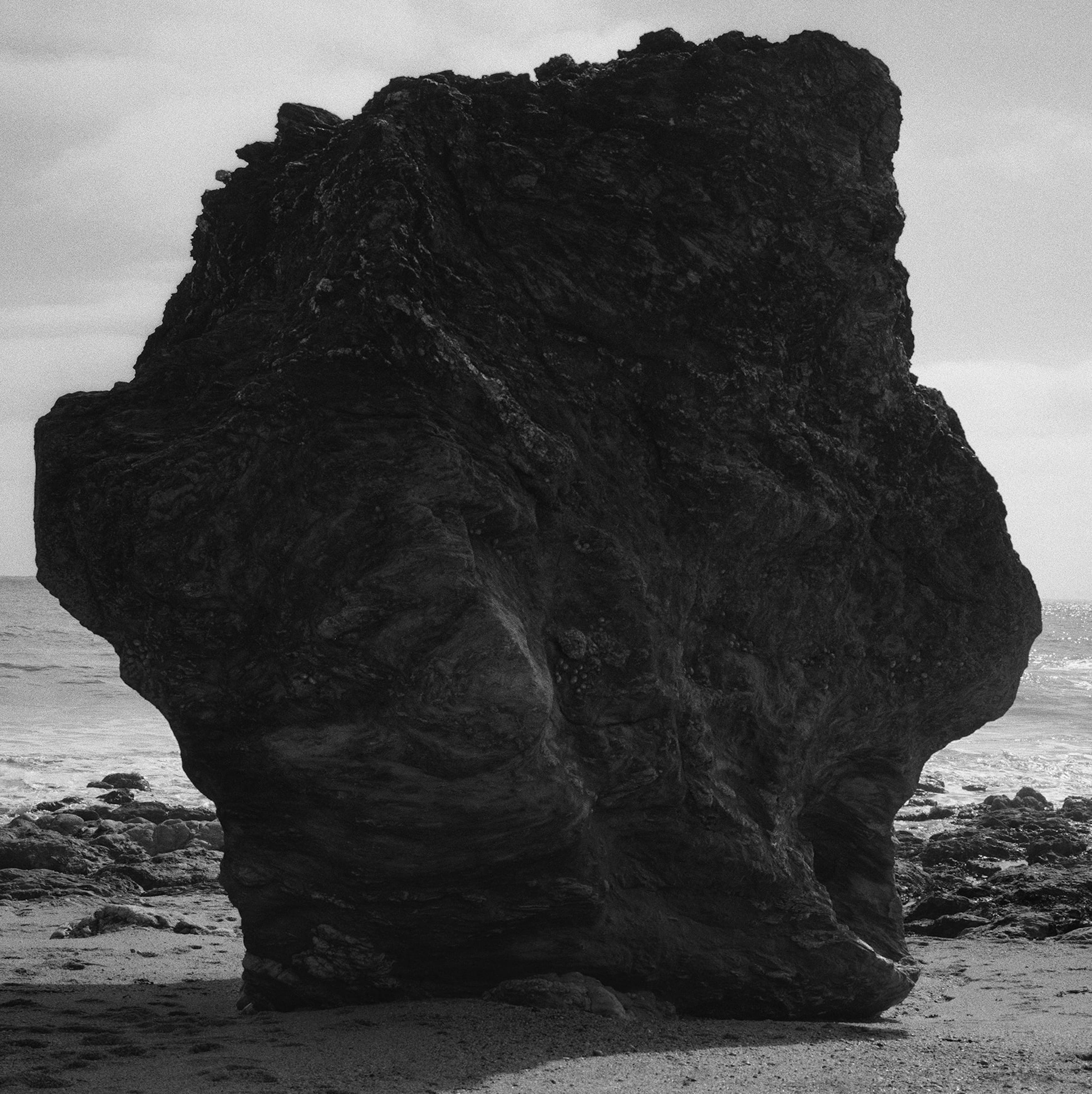 a large black boulder on the ocean shore