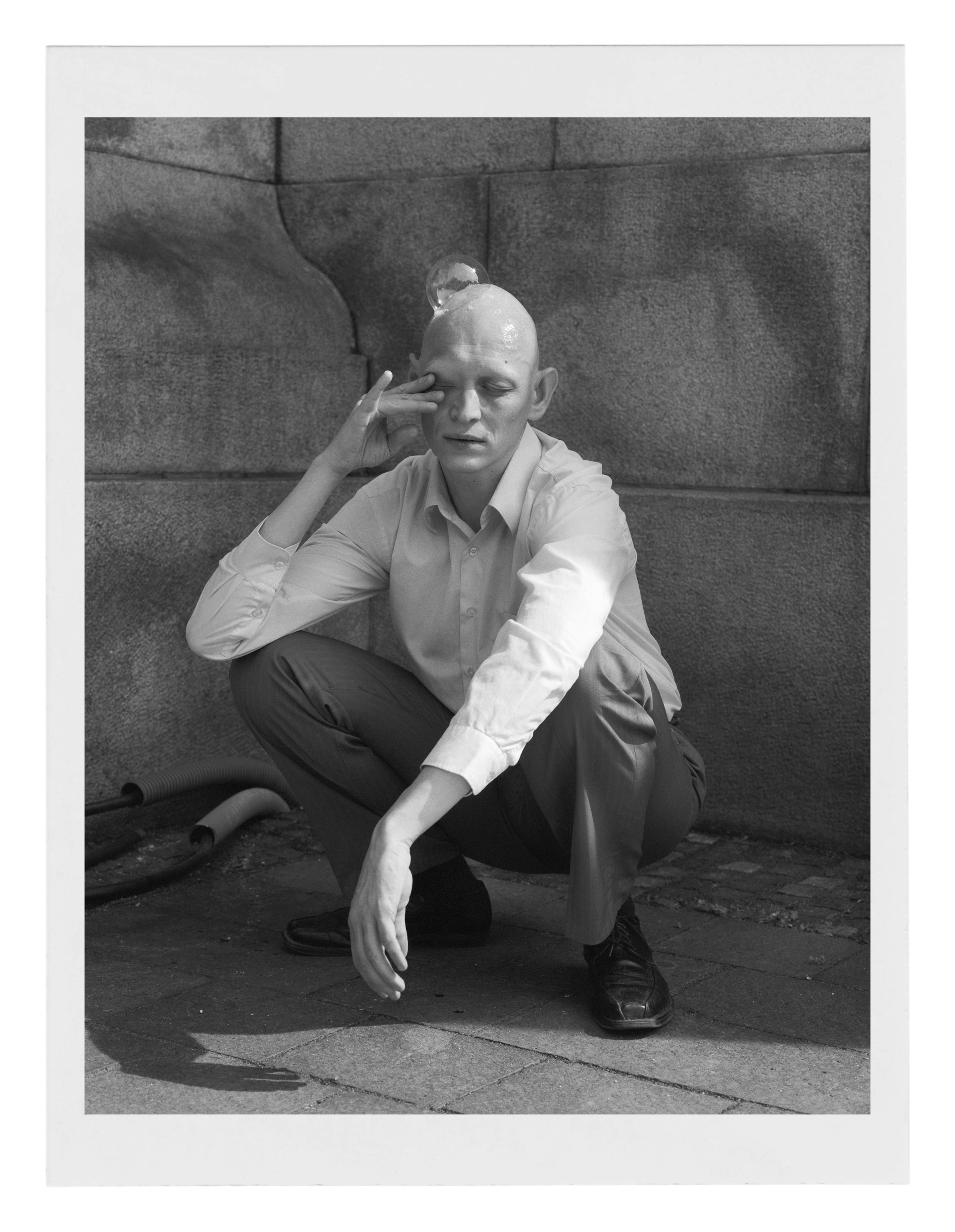 a bold squatting man with a  soap bubble on his head