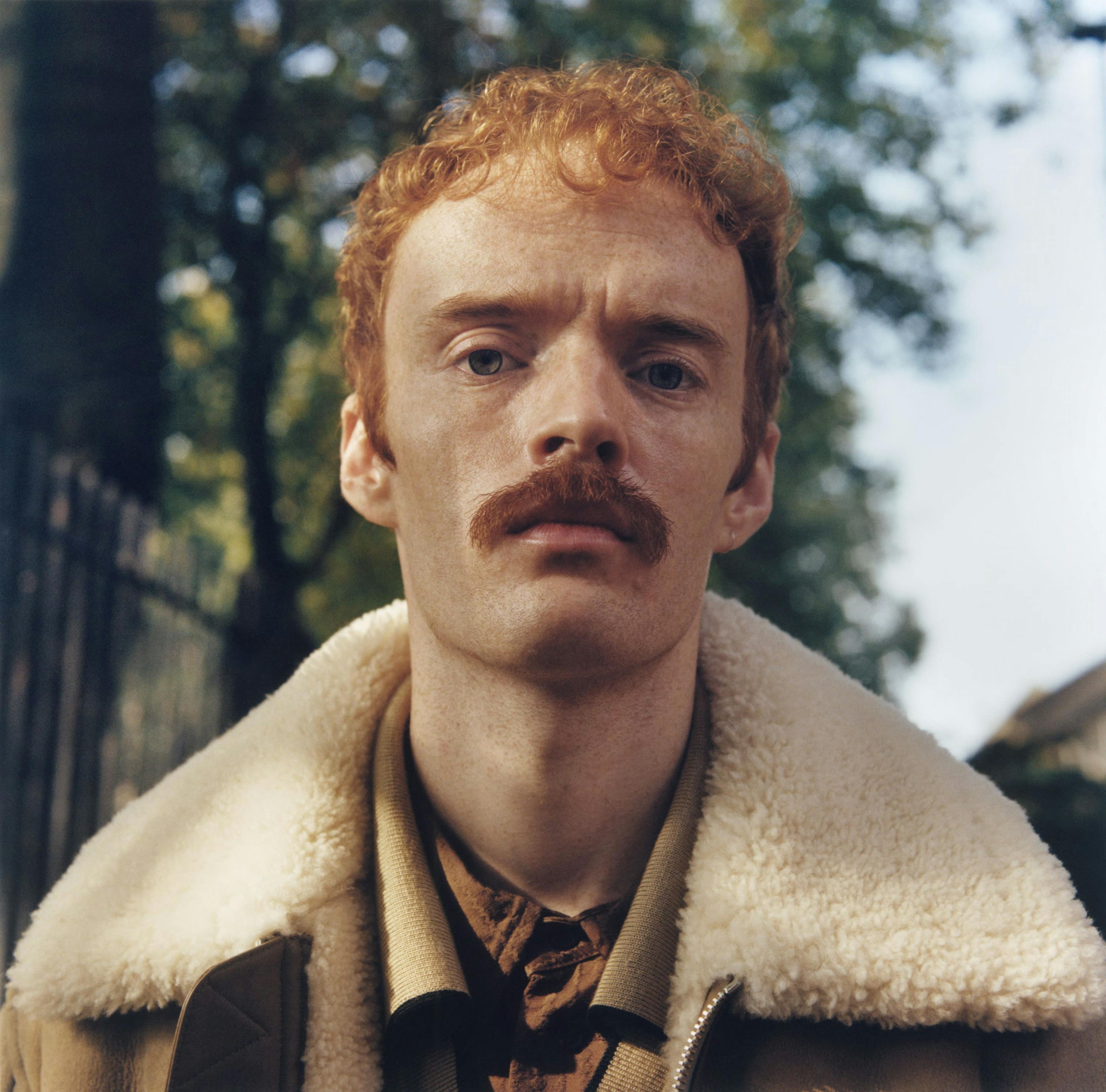 a man with a moustache standing in a park