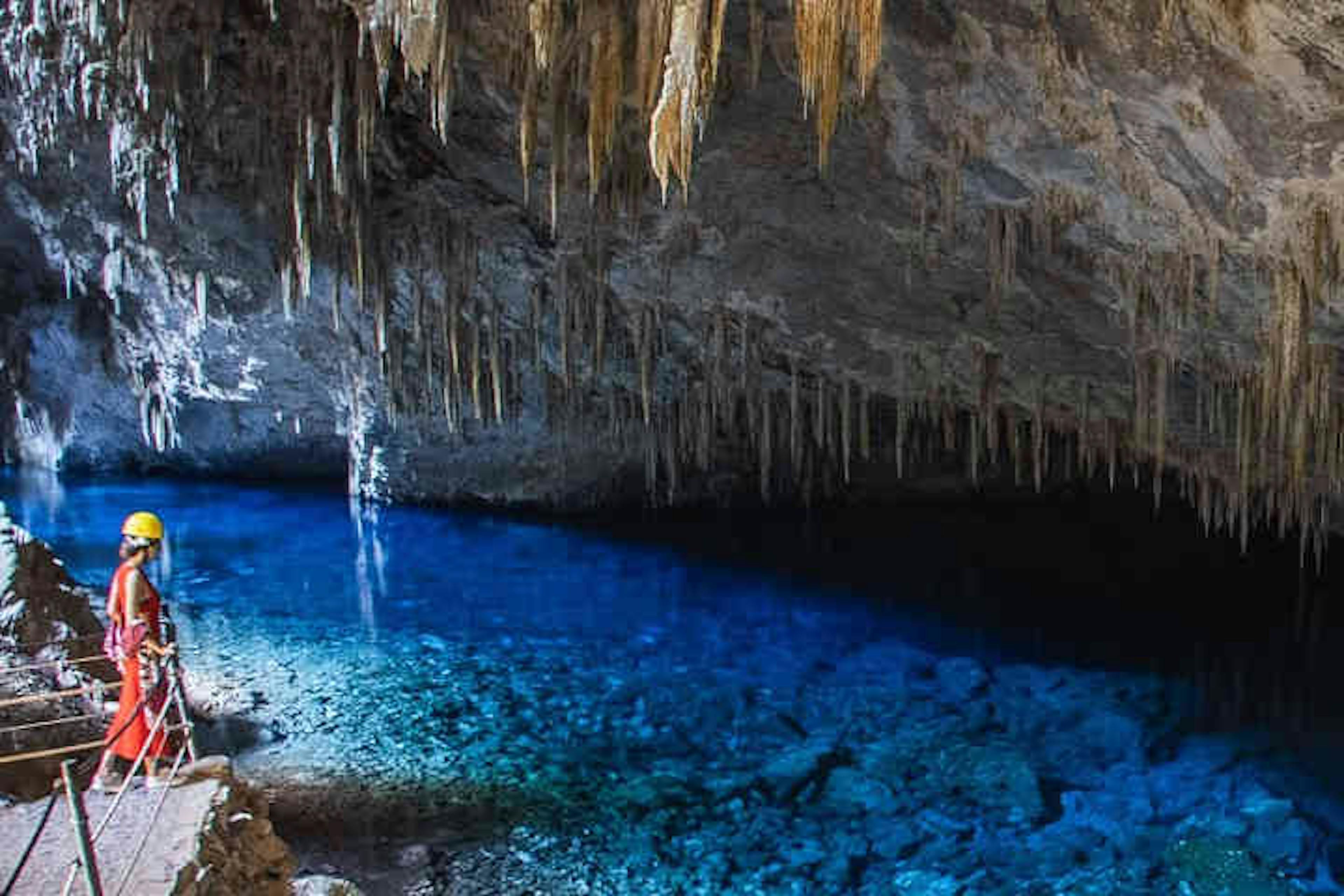 Turista contemplando lago azul dentro da gruta