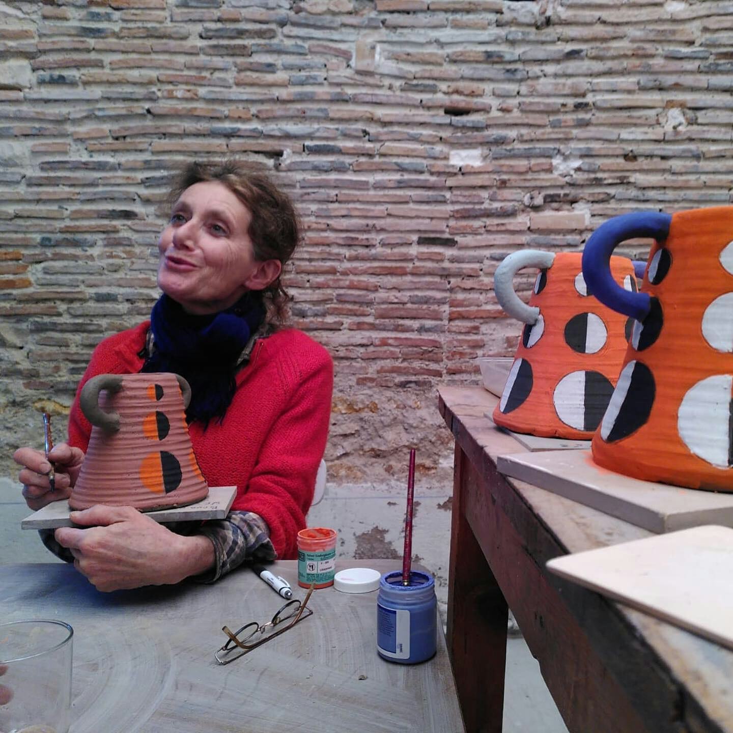 A woman paints a pot with ceramic glaze. Two more glazed pots sit to the side