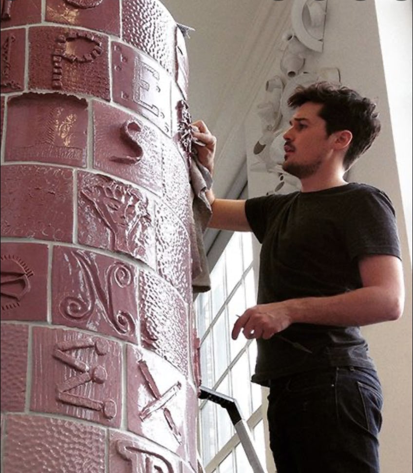 Matthew Raw works on a large artwork covered in dark pink tiles