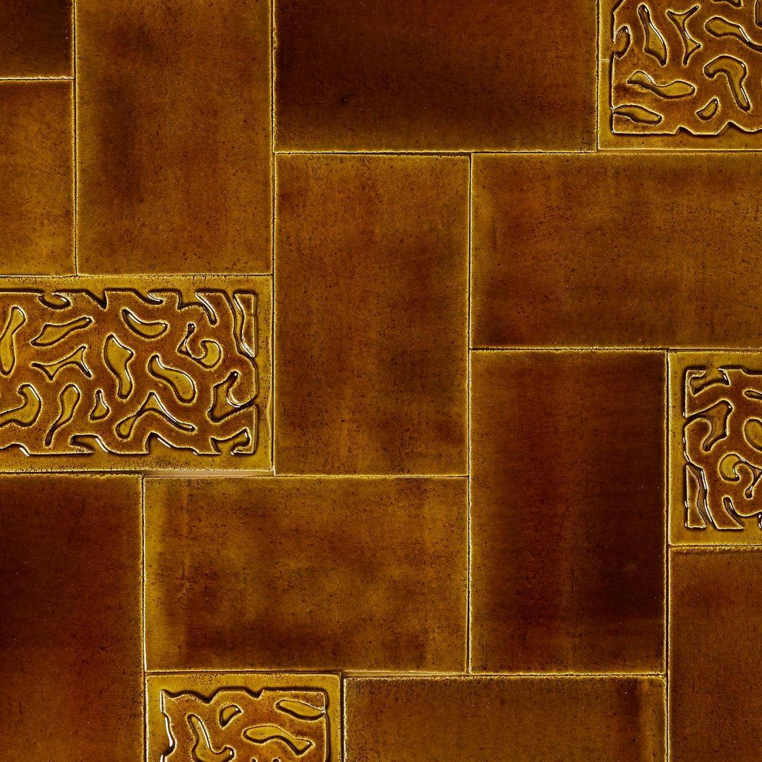 Brown glazed tiles laid in a herringbone pattern. Most of the tiles are smooth but a few have a fluid pattern cut out of them