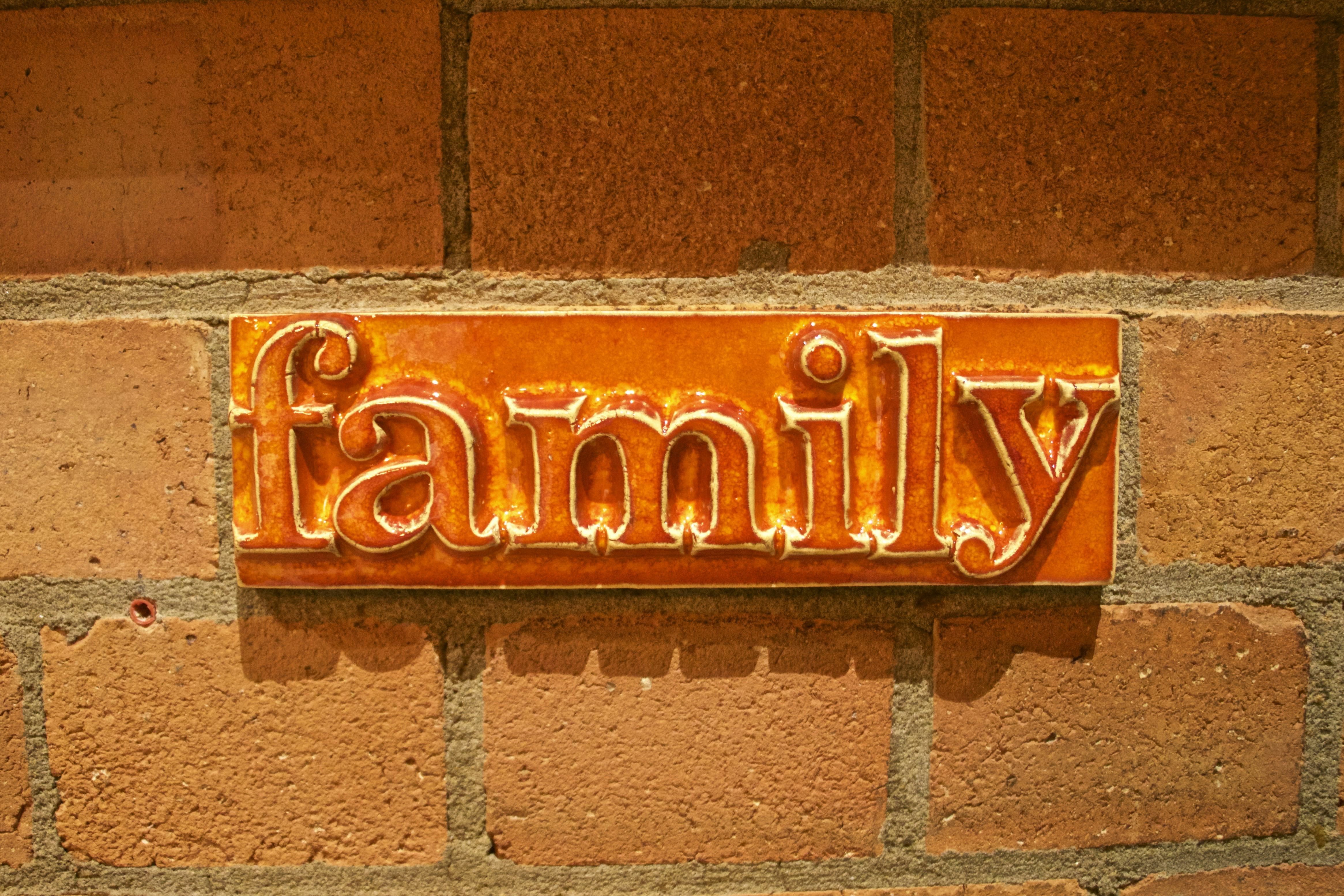 an orange ceramic tile with the word ‘family’ embossed hangs on a red brick wall