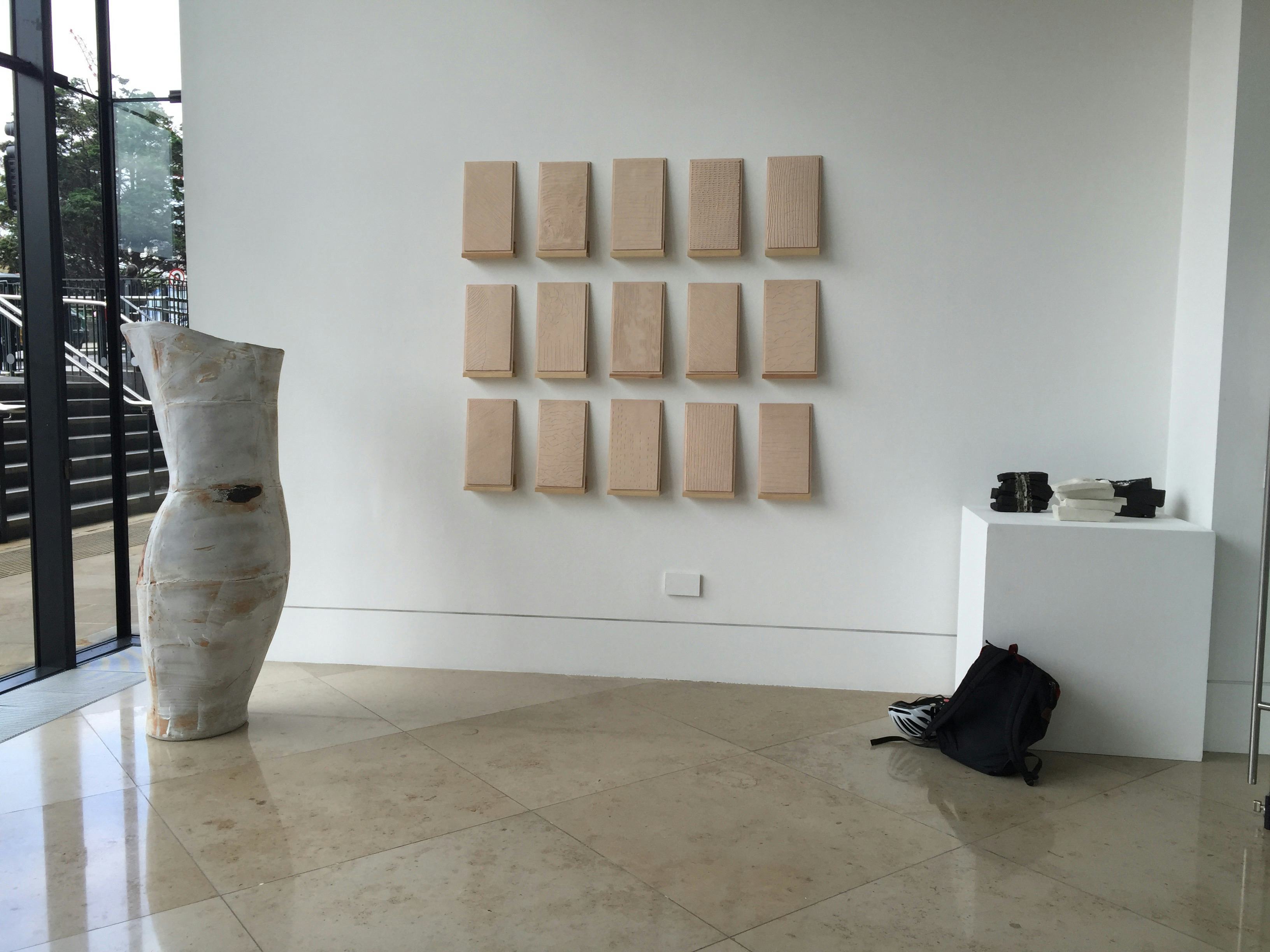 Three rows of 5 tiles sit on individual plinths on a wall alongside other artworks