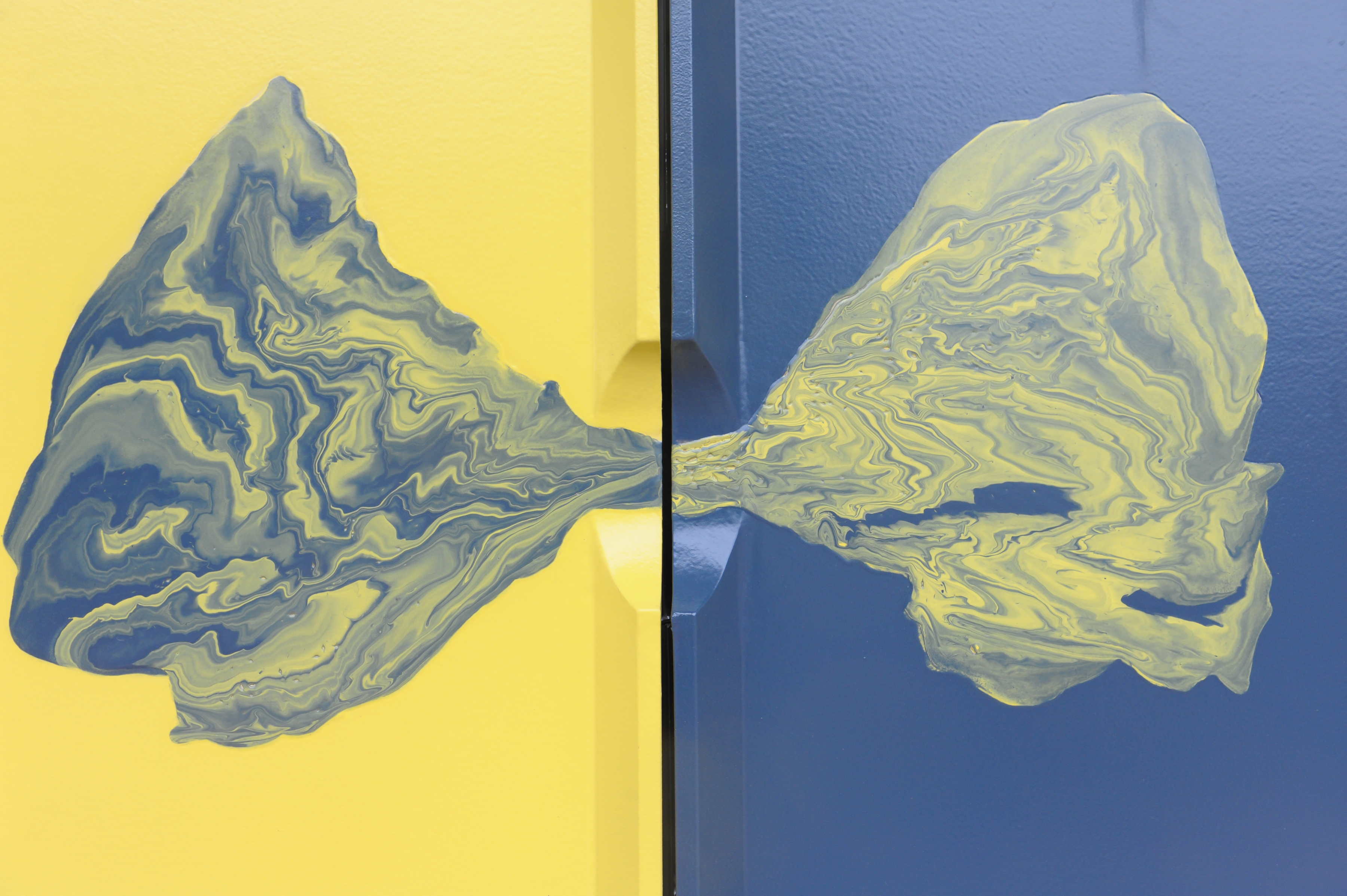 A detail of a yellow tile and a blue tile. The colours appear to be flowing from tile to the other and mixing together