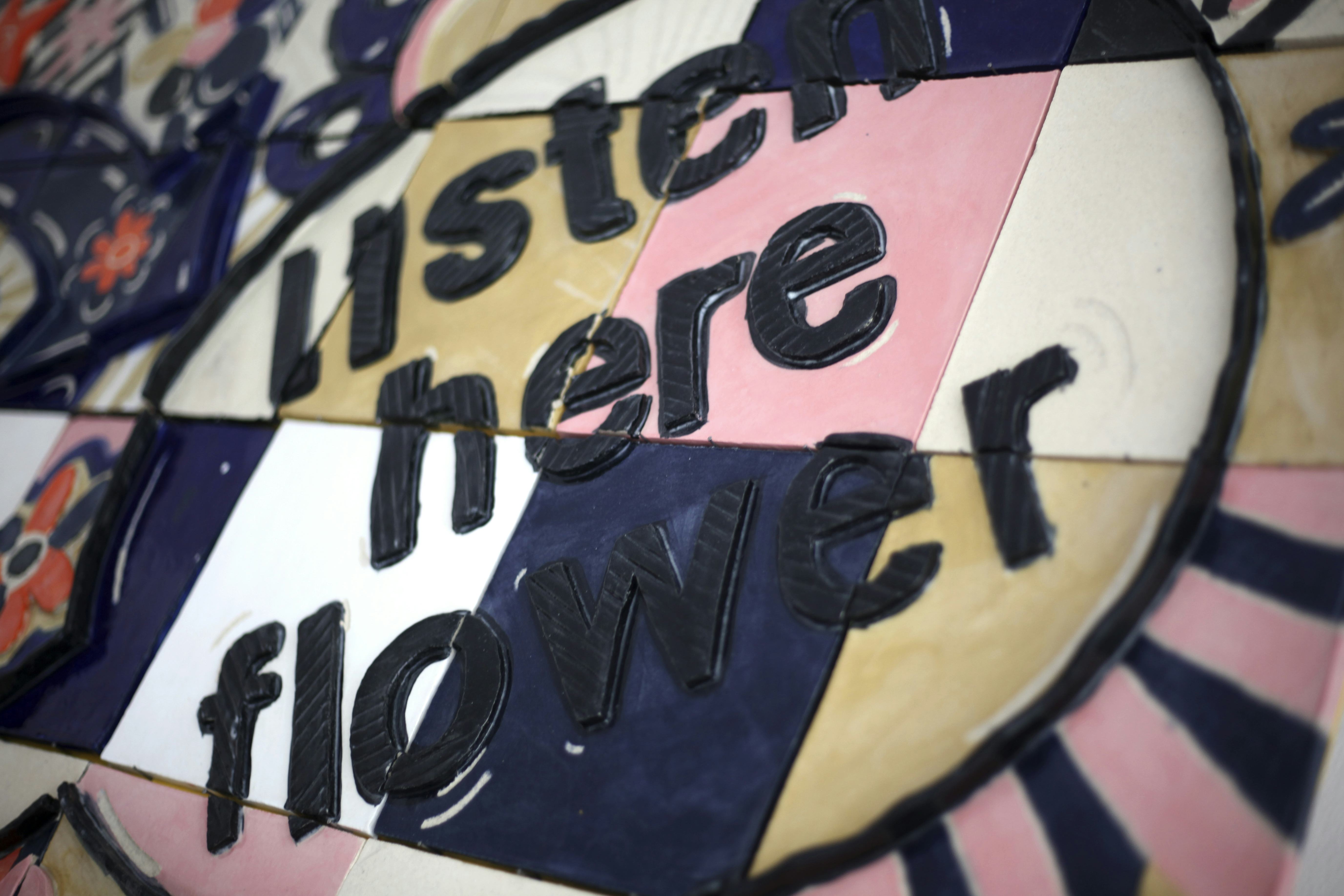 A detail of a colourful tiled mural with the words ‘listen here flower’